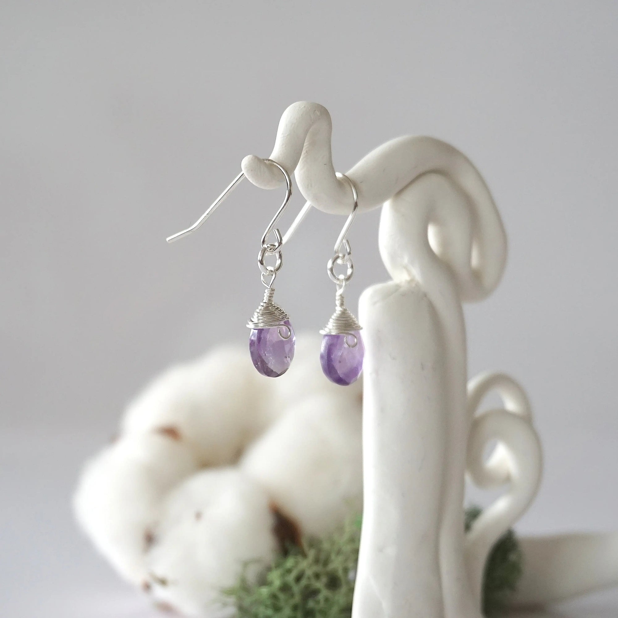 Side view of amethyst sterling silver drop earrings showing wire wrapped natural faceted amethyst, artisan craftsmanship, on a display – Designs by Nature Gems