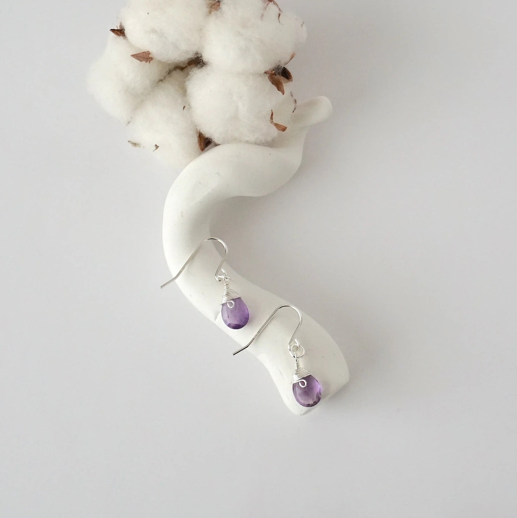 Amethyst sterling silver drop earrings with faceted natural amethyst stones and wire wrapping, laying flat on a display – Designs by Nature Gems