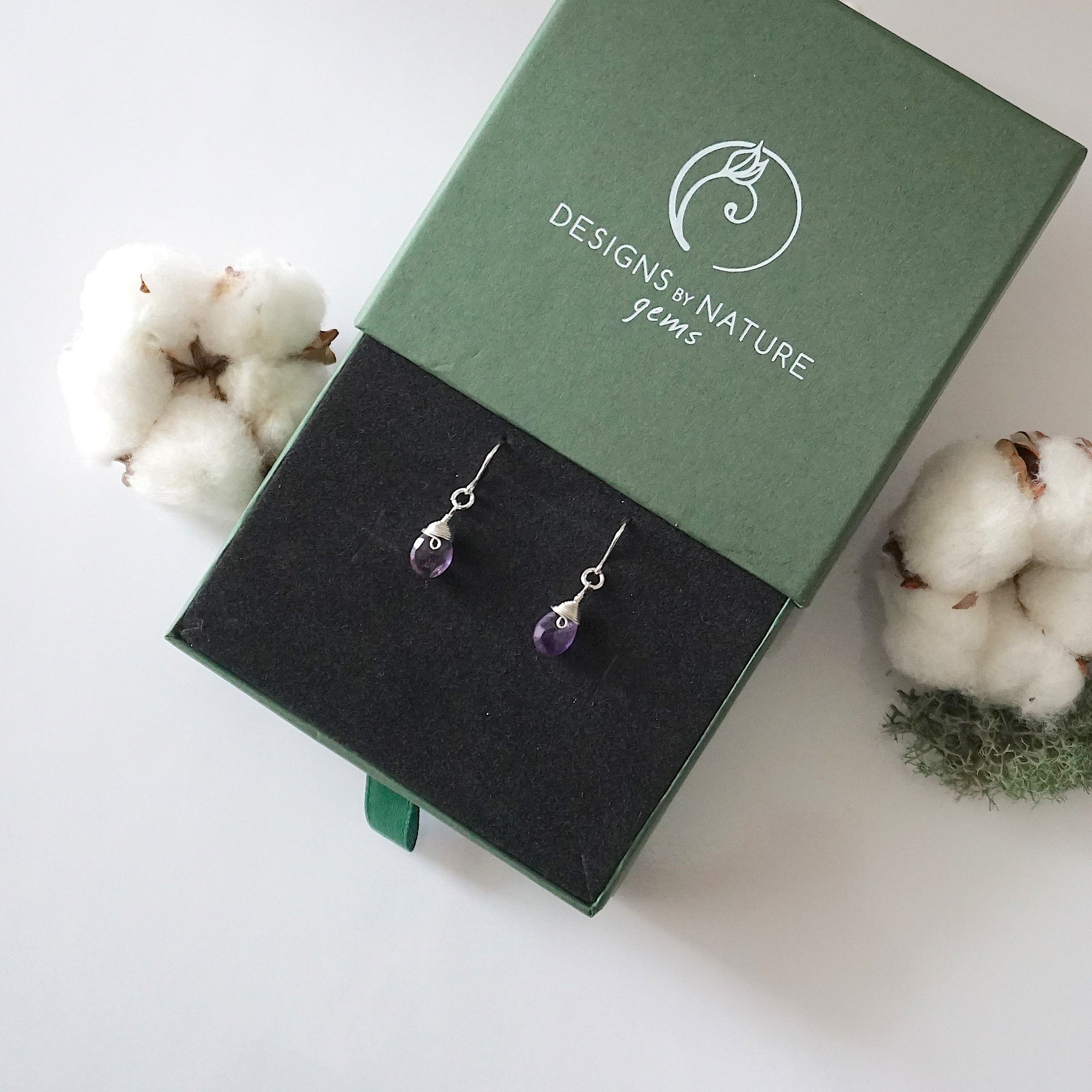 Amethyst sterling silver drop earrings in branded Designs by Nature Gems jewelry box, showcasing handcrafted faceted amethyst and sterling silver wire wrapping