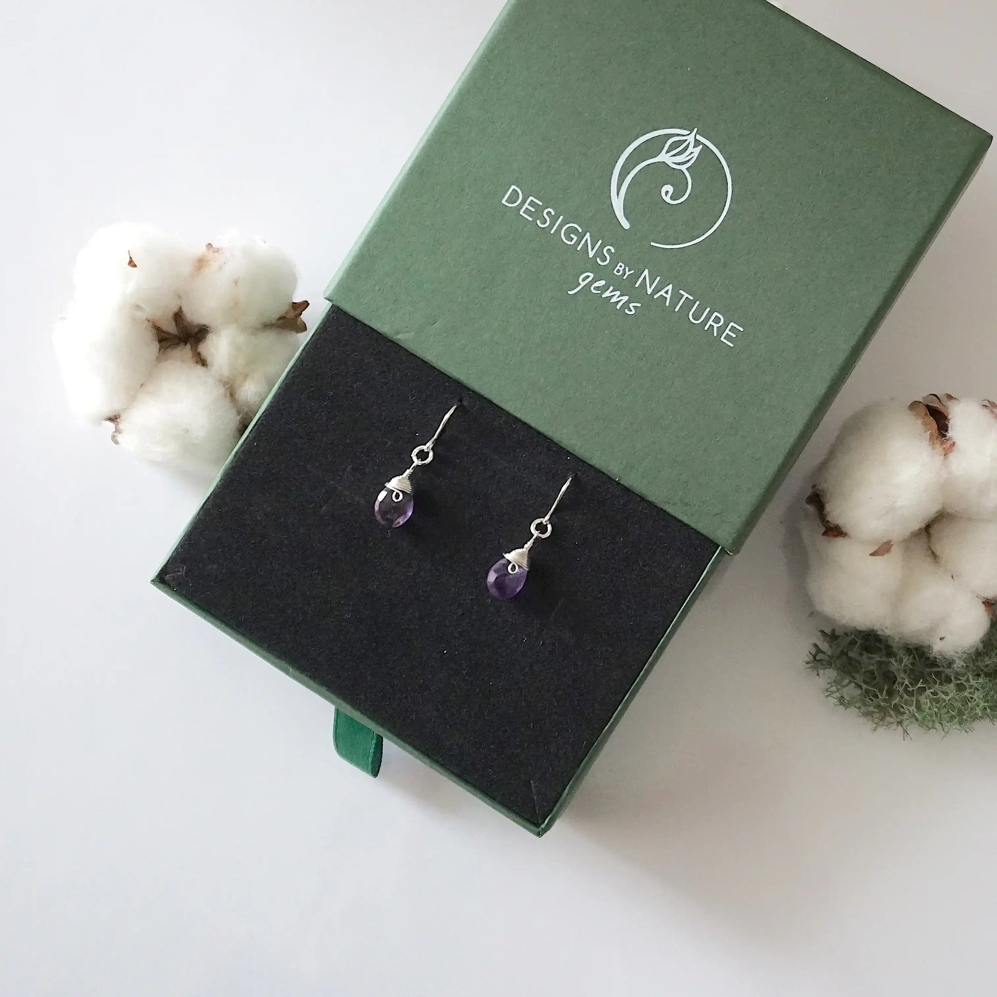 Amethyst sterling silver drop earrings in branded Designs by Nature Gems jewelry box, showcasing handcrafted faceted amethyst and sterling silver wire wrapping