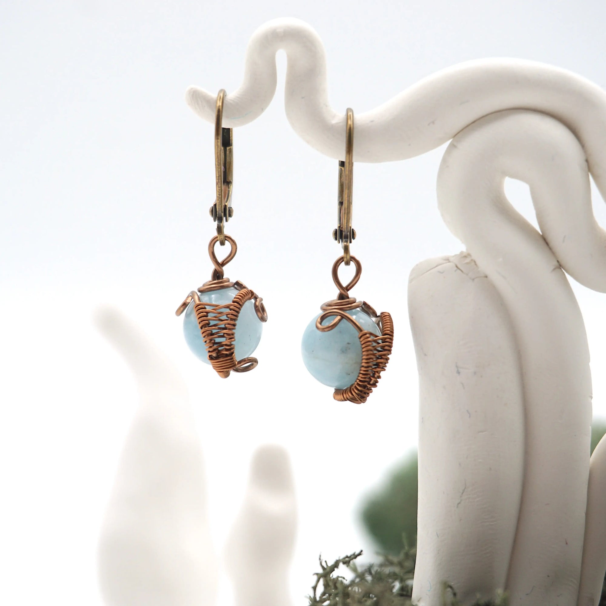Close-up of handcrafted aquamarine drop earrings with antique bronze copper wire wrapping.