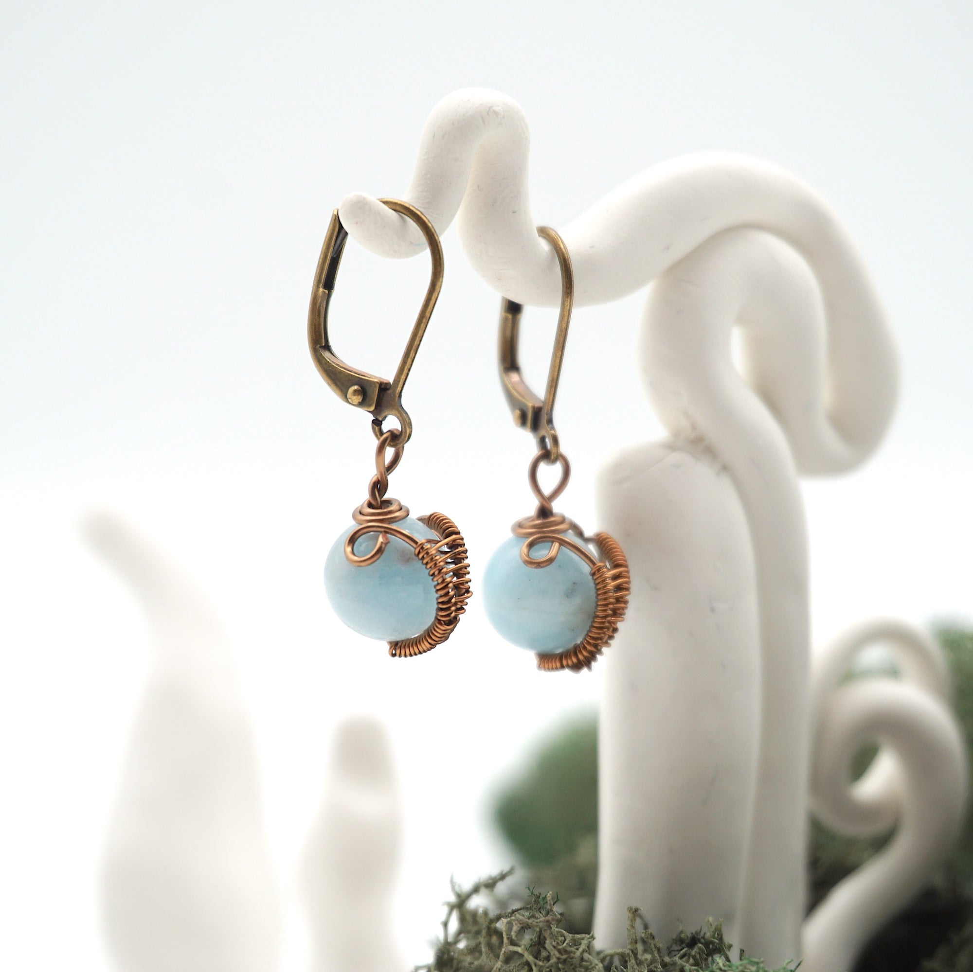 Side angle of aquamarine drop earrings on a display stand, highlighting antique bronze copper wire wrapping.