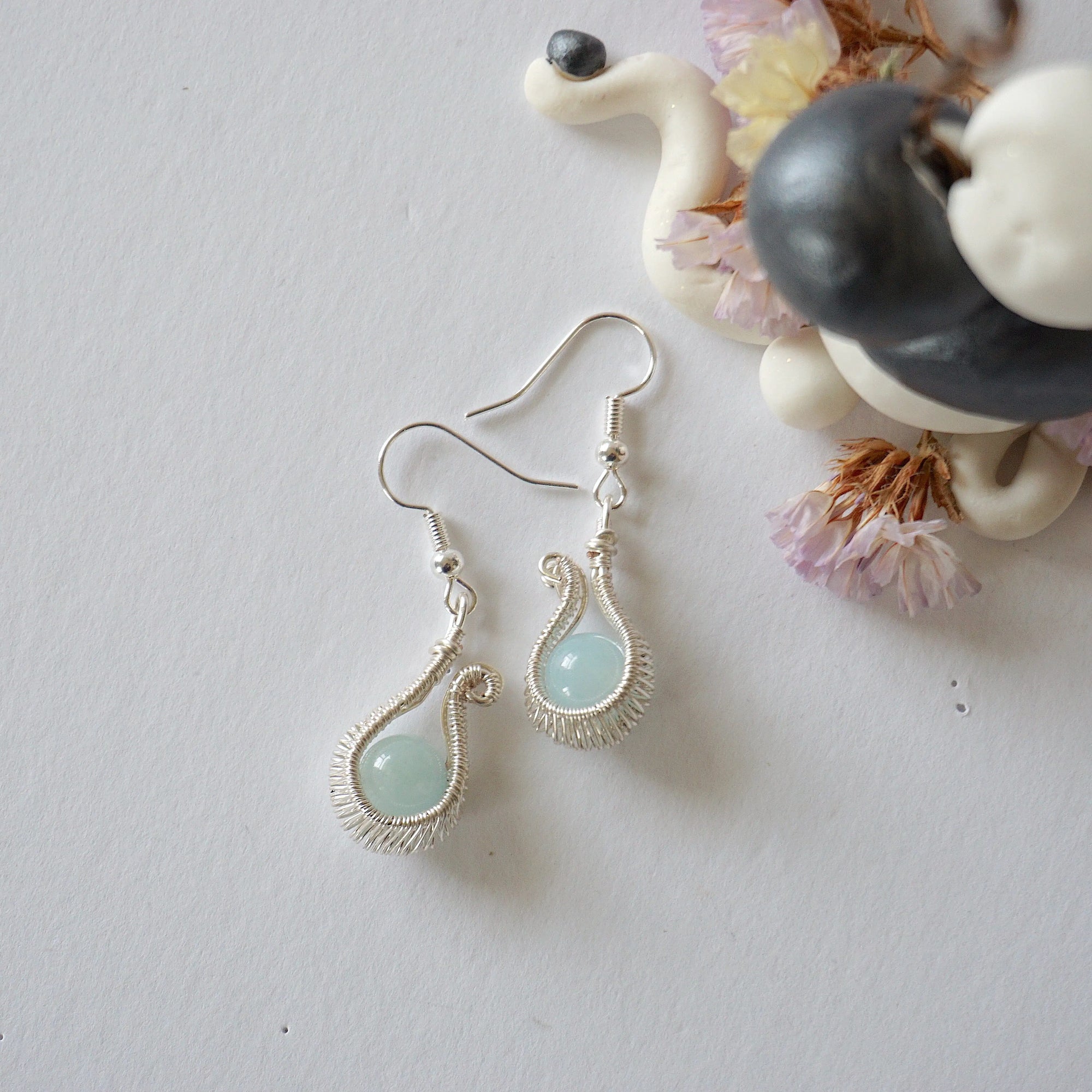 Aquamarine drop earring laying flat, displaying full pendant and fish hook, soft silver finish