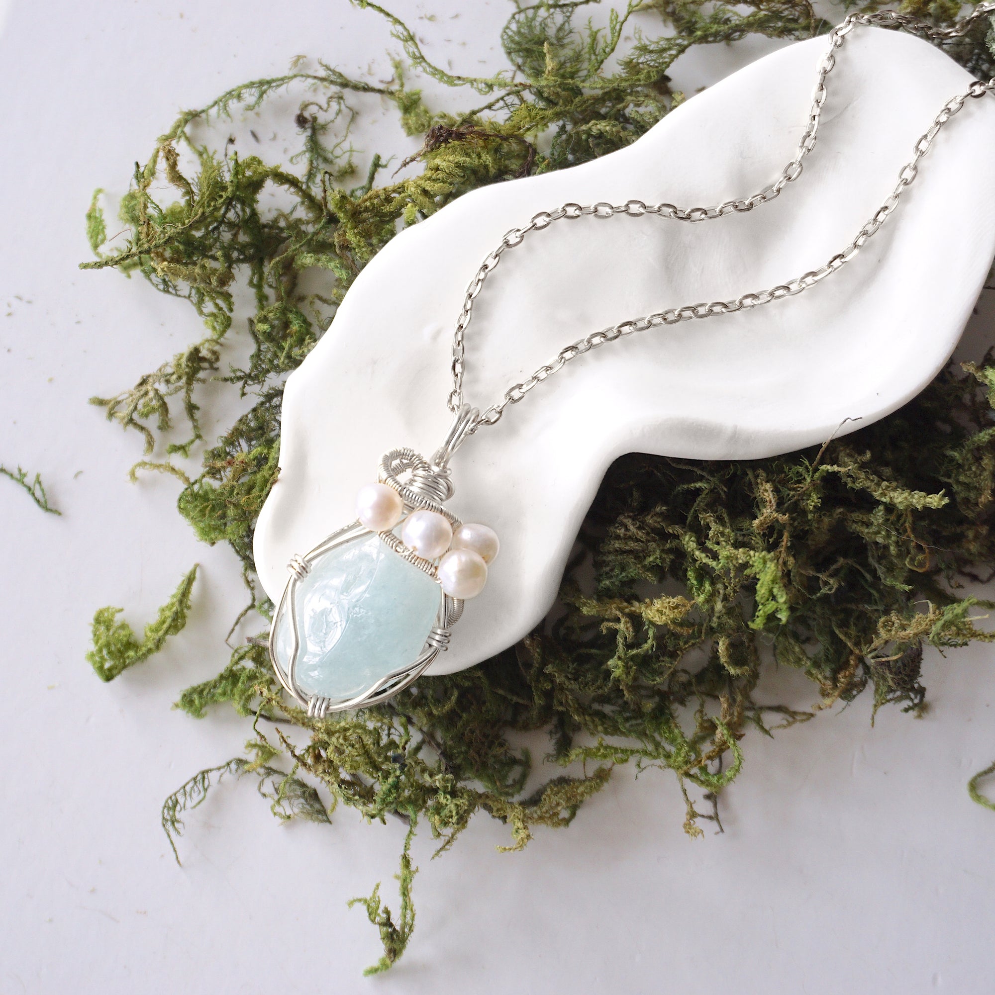 Handmade silver wire wrapped aquamarine and freshwater pearl necklace laying flat on a silver plated chain, artisan jewelry for women