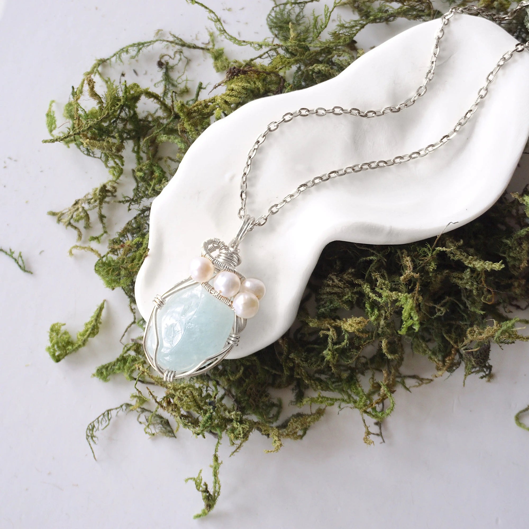 Handmade silver wire wrapped aquamarine and freshwater pearl necklace laying flat on a silver plated chain, artisan jewelry for women