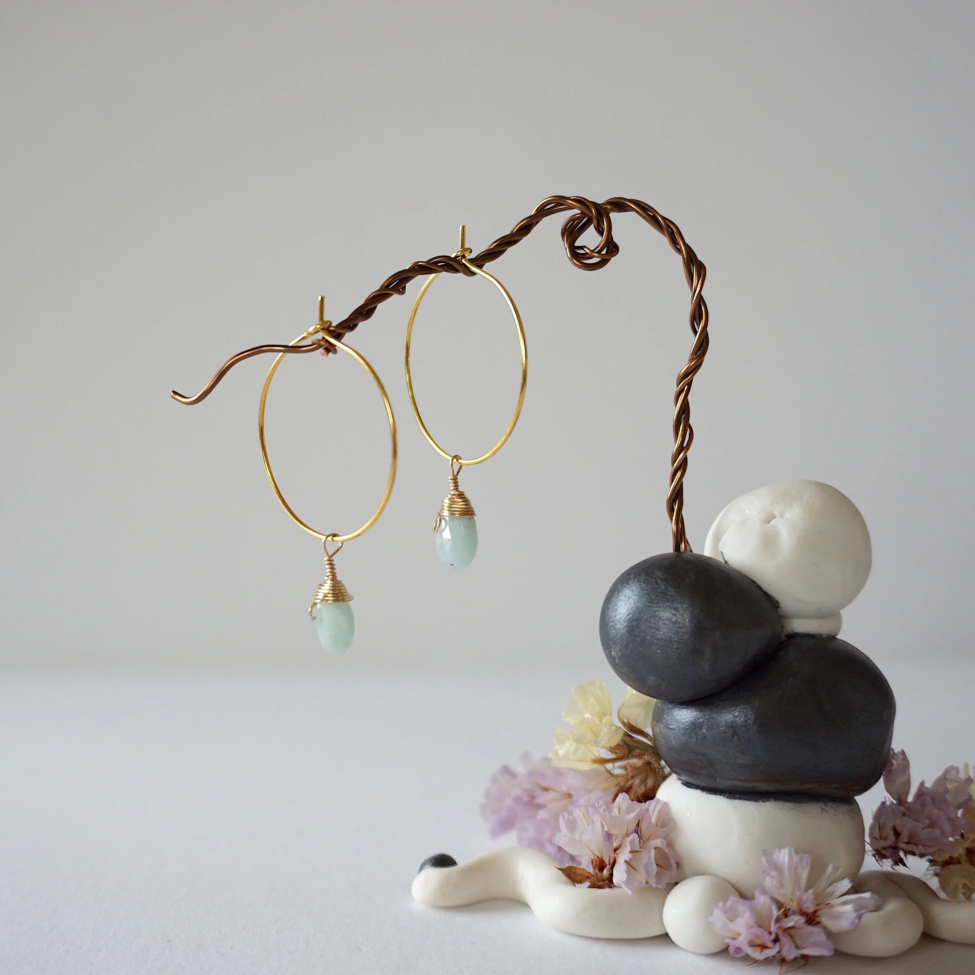 Angled view of gold plated aquamarine hoop earrings with wire wrapped gemstone drops, showing faceted March birthstone detail