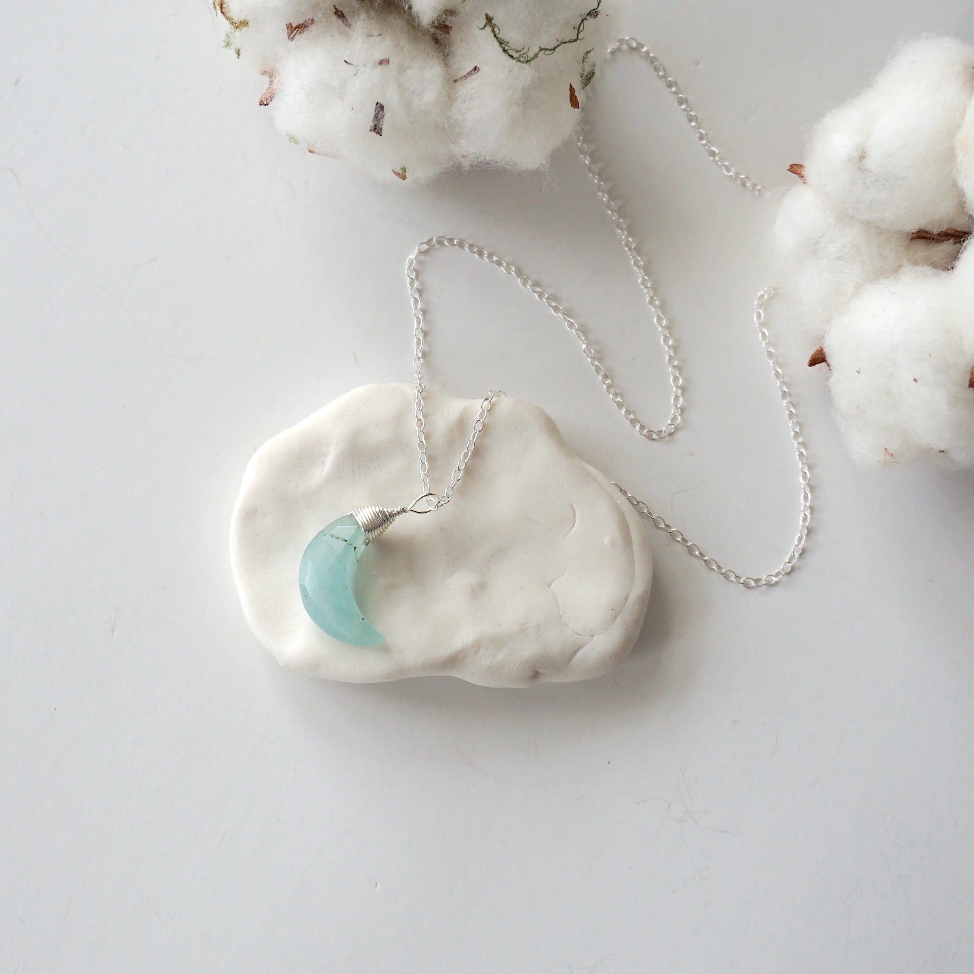 Aquamarine moon necklace laying flat, showing crescent shape and sterling silver chain, minimalist artisan design