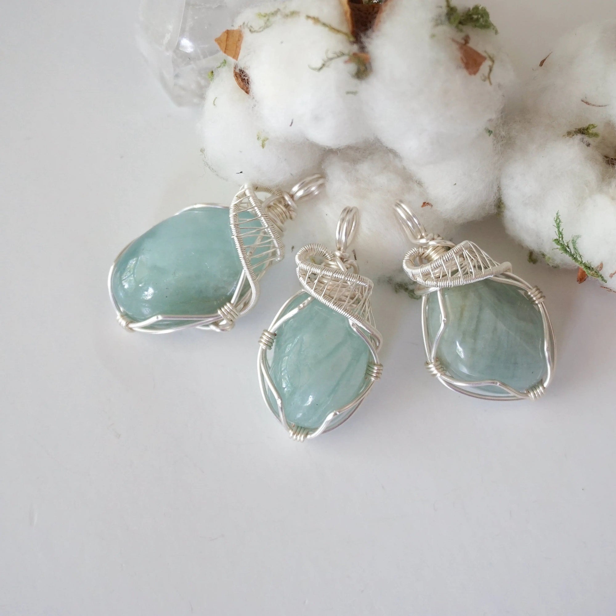 Three aquamarine pendants showing natural variation in size, shape, and blue color, artisan wire wrapped, soft silver over copper