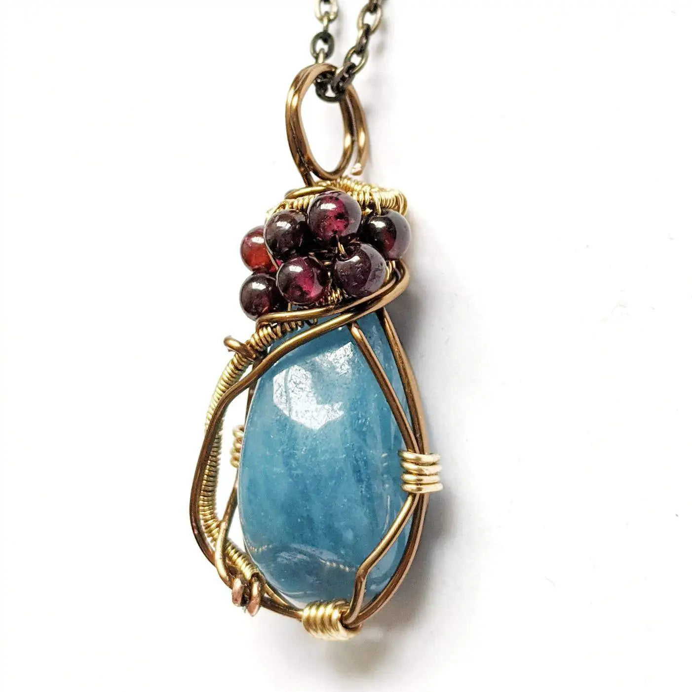 Front view of an aquamarine pendant necklace with garnet accents on an antique bronze chain
