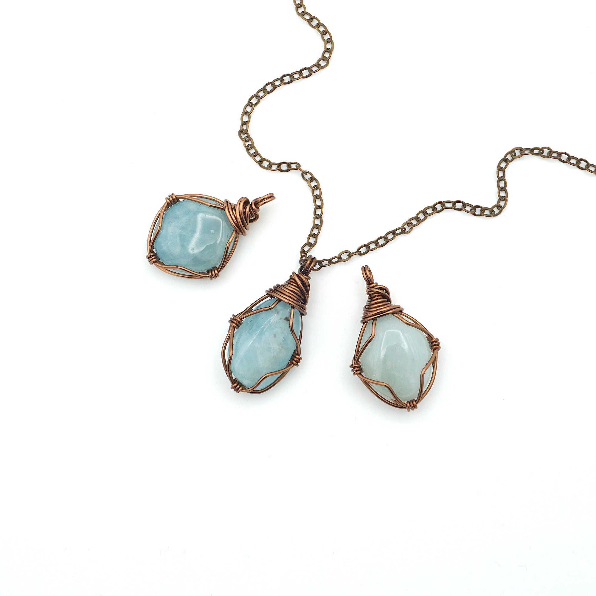 Three aquamarine pendants showing natural variation in size, shape, and blue color with antique bronze wire wrapping