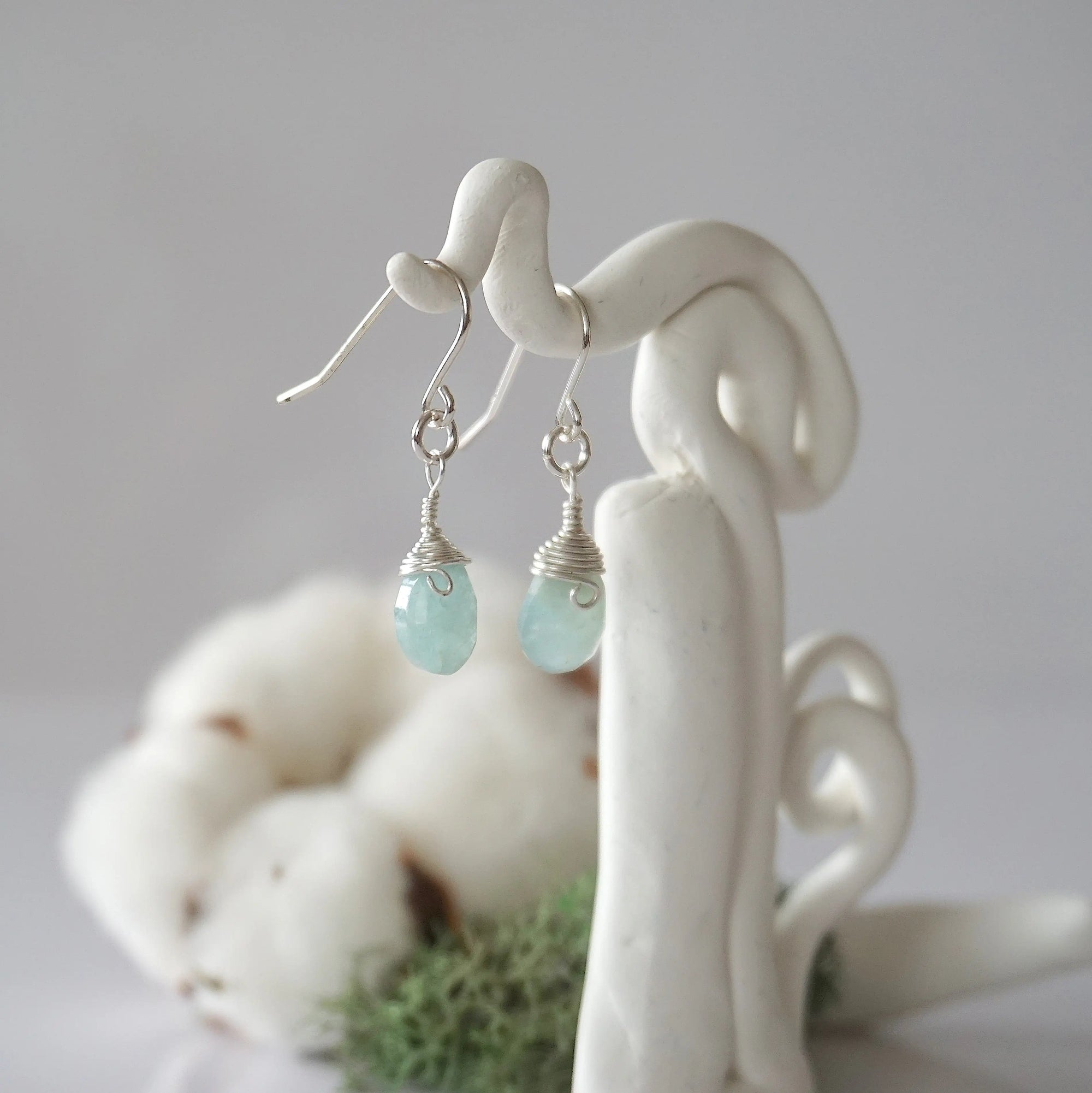 Side view of aquamarine sterling silver drop earrings showing wire wrapped natural faceted aquamarine, artisan craftsmanship, on a display – Designs by Nature Gems