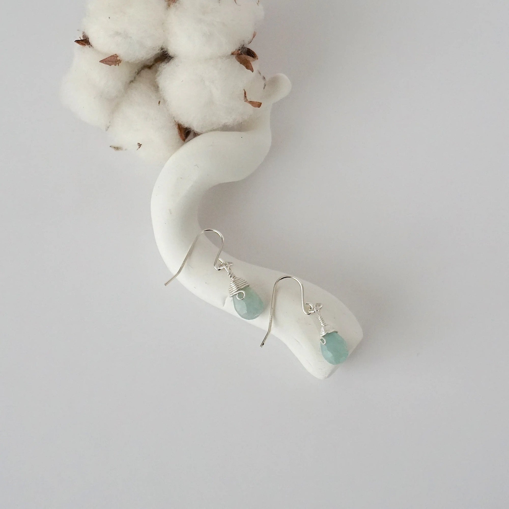 Aquamarine sterling silver drop earrings with faceted natural aquamarine stones and wire wrapping, laying flat on a display – Designs by Nature Gems