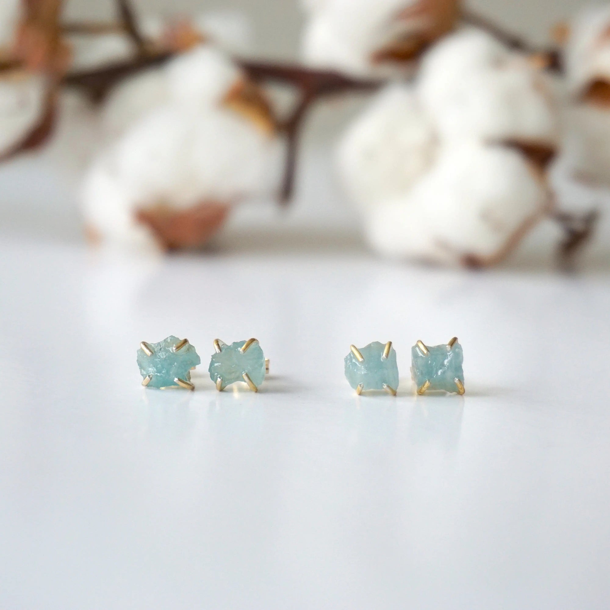 Two pairs of raw aquamarine stud earrings showing natural variation in size, shape, and blue color, Designs by Nature Gems