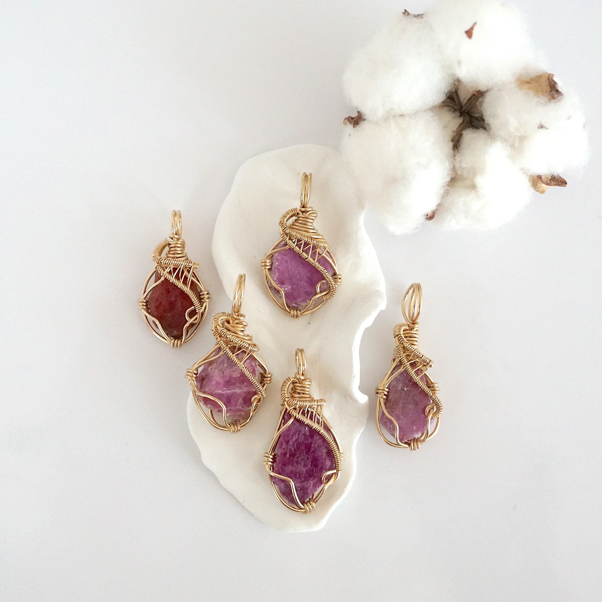 Five raw pink ruby pendants in 14k gold filled, showing natural variation in size, shape, and color. Handcrafted July birthstone jewelry by Designs by Nature Gems.
