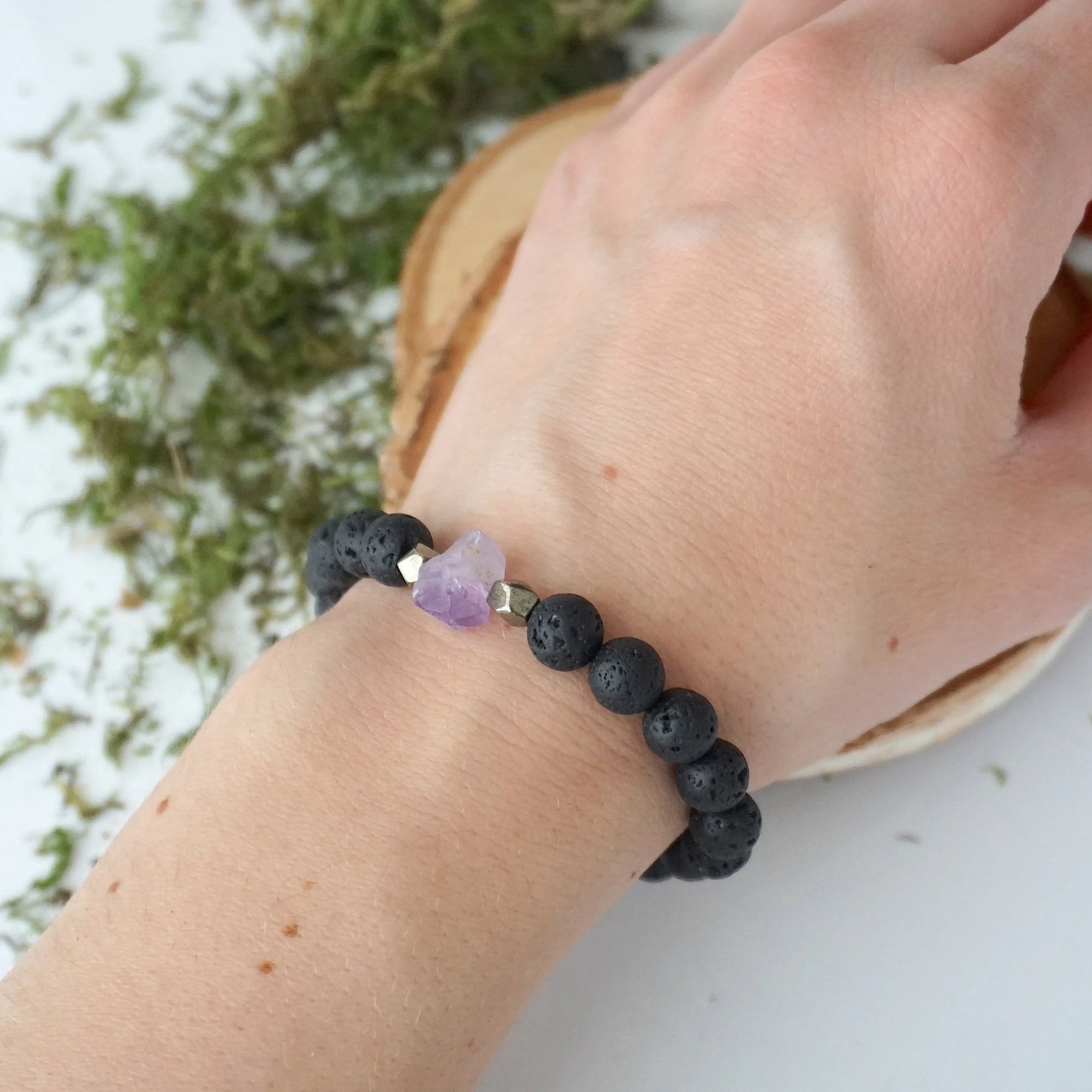 Black lava beaded bracelet on woman's wrist with raw amethyst crystal and pyrite accents, unisex stretch fit
