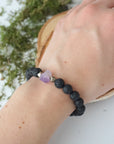 Black lava beaded bracelet on woman's wrist with raw amethyst crystal and pyrite accents, unisex stretch fit