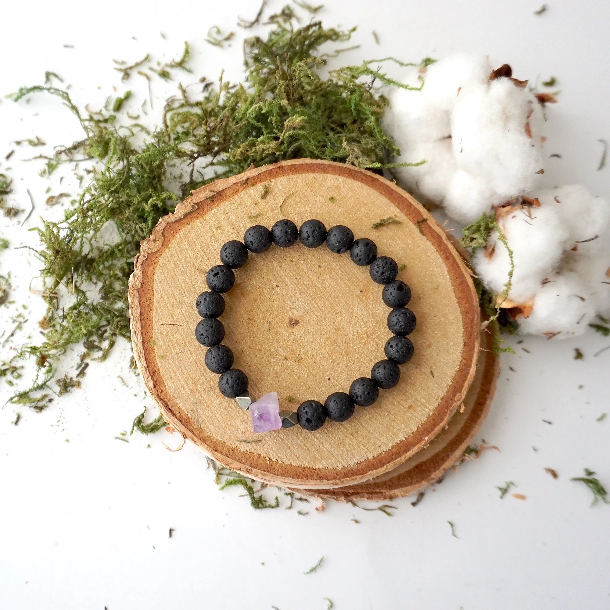 Top view of black lava stone bracelet with raw amethyst centerpiece and pyrite accents on stretch cord