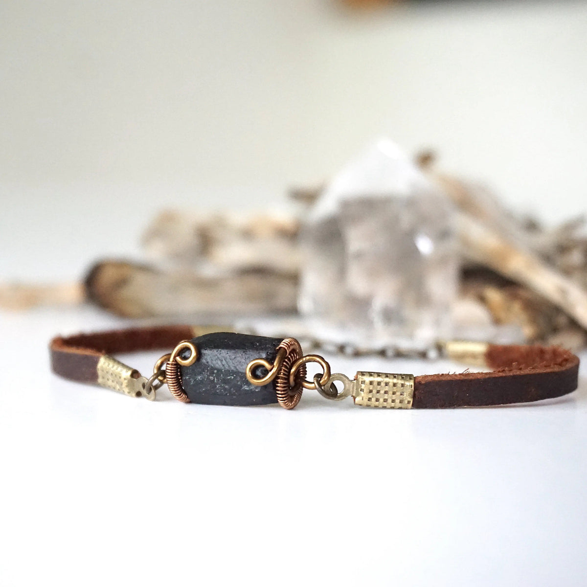 Close-up of natural black tourmaline hand wire-wrapped in antique bronze on a brown leather band