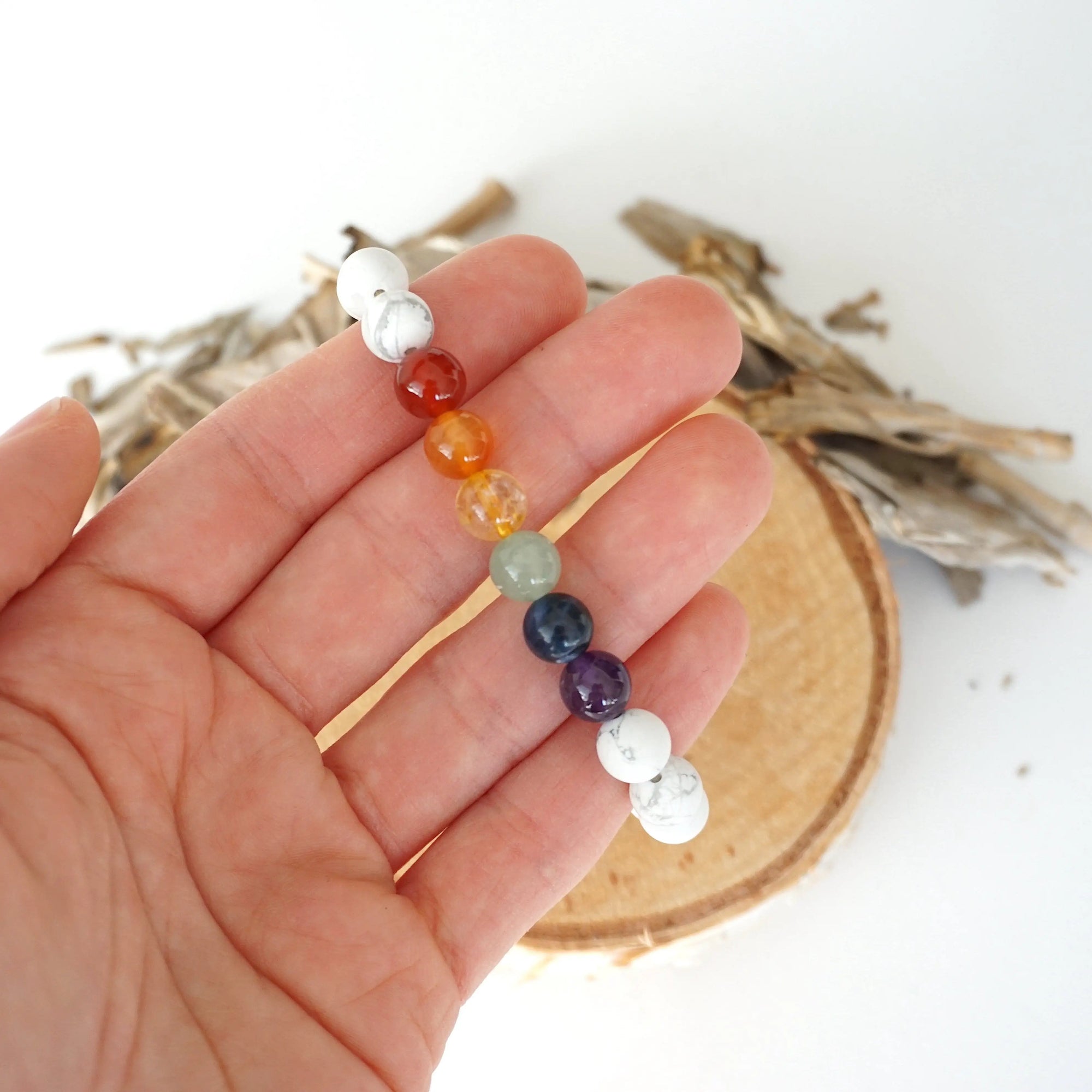 Chakra beaded stretch bracelet in hand for size reference, natural white howlite, amethyst, lapis lazuli, green aventurine, citrine, orange carnelian, red carnelian beads