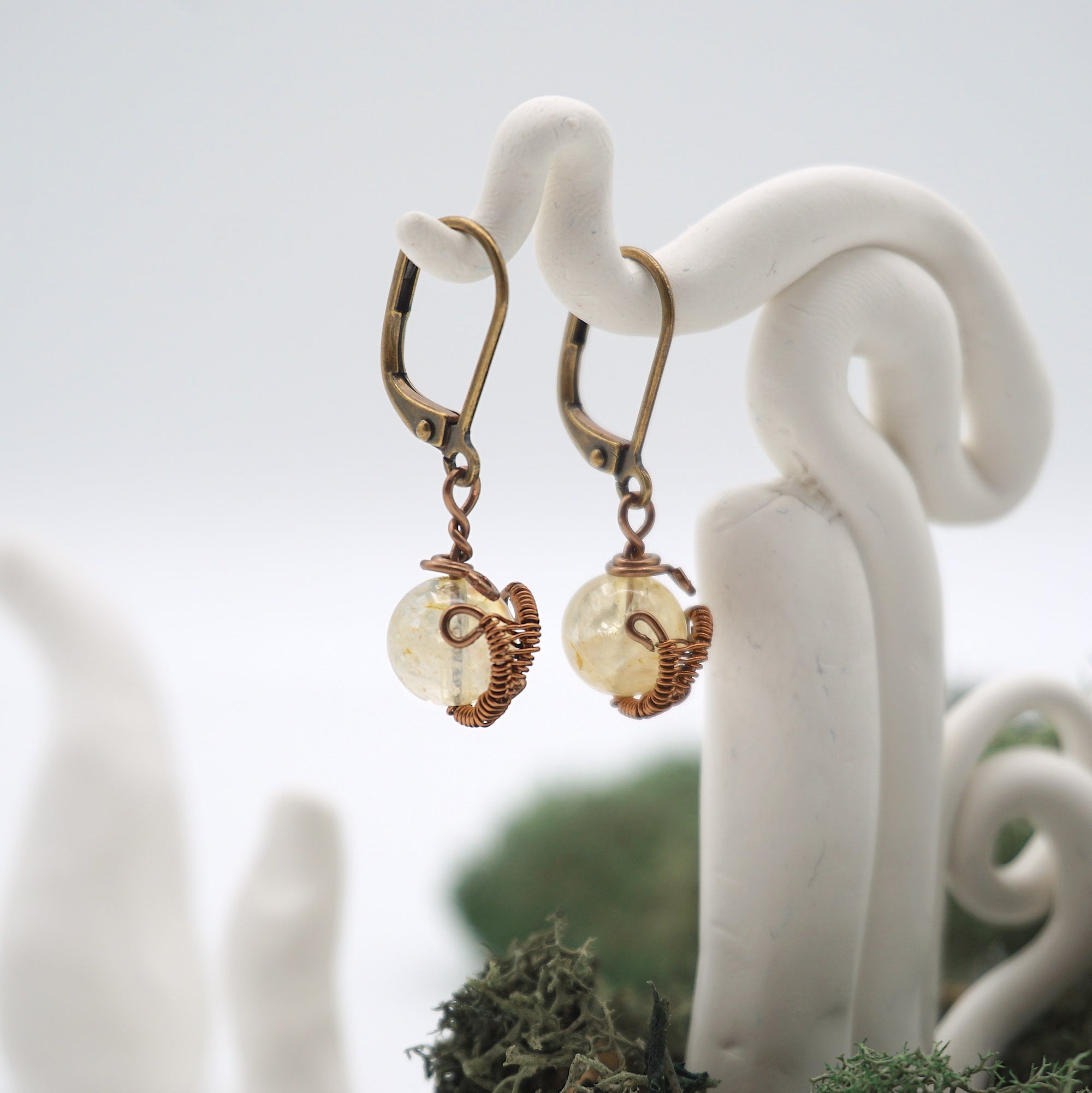 Side angle of citrine drop earrings on a display stand, highlighting antique bronze copper wire wrapping.