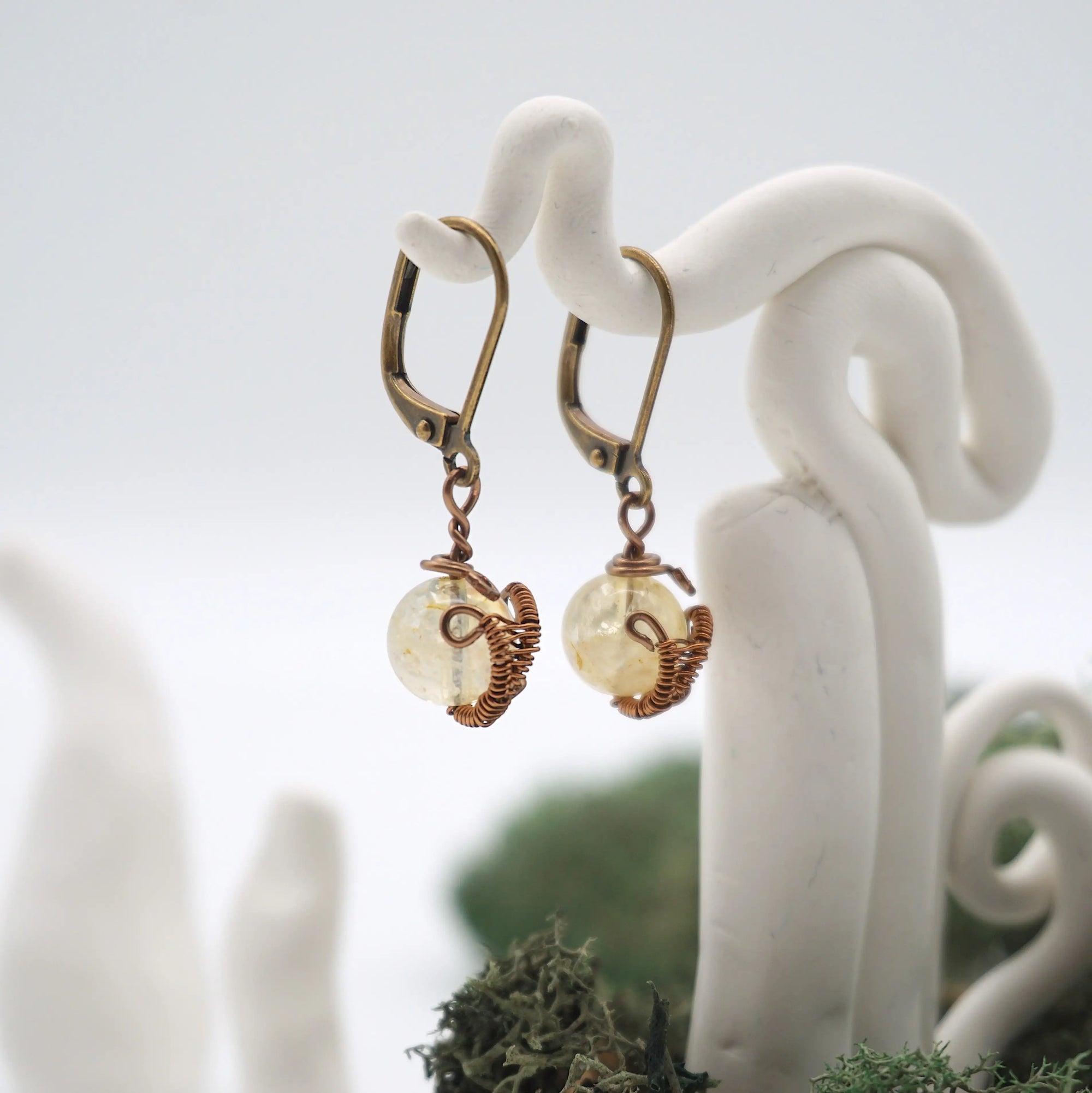 Side angle of citrine drop earrings on a display stand, highlighting antique bronze copper wire wrapping.