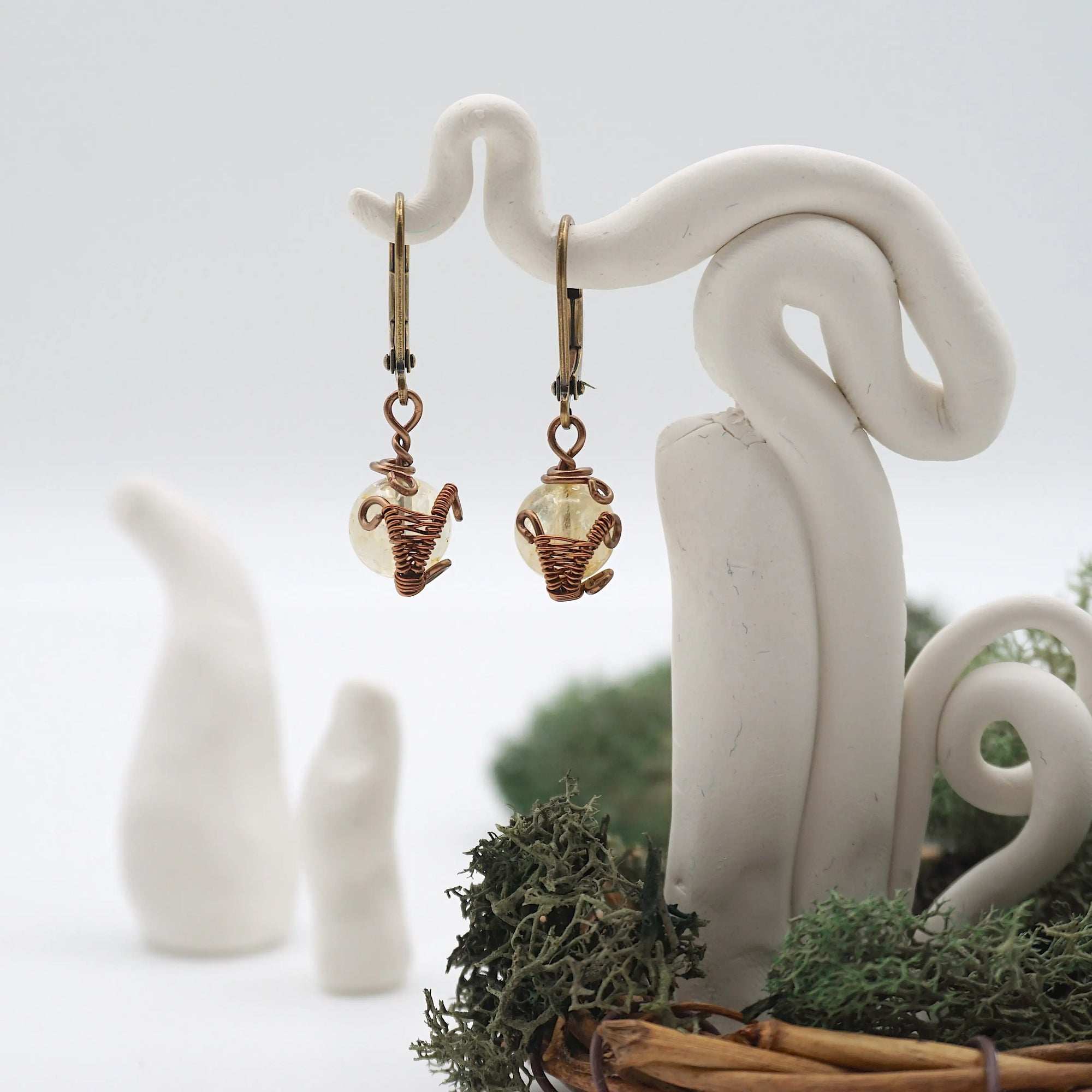 Front angle of citrine drop earrings hanging on a jewelry display, wire-wrapped design.