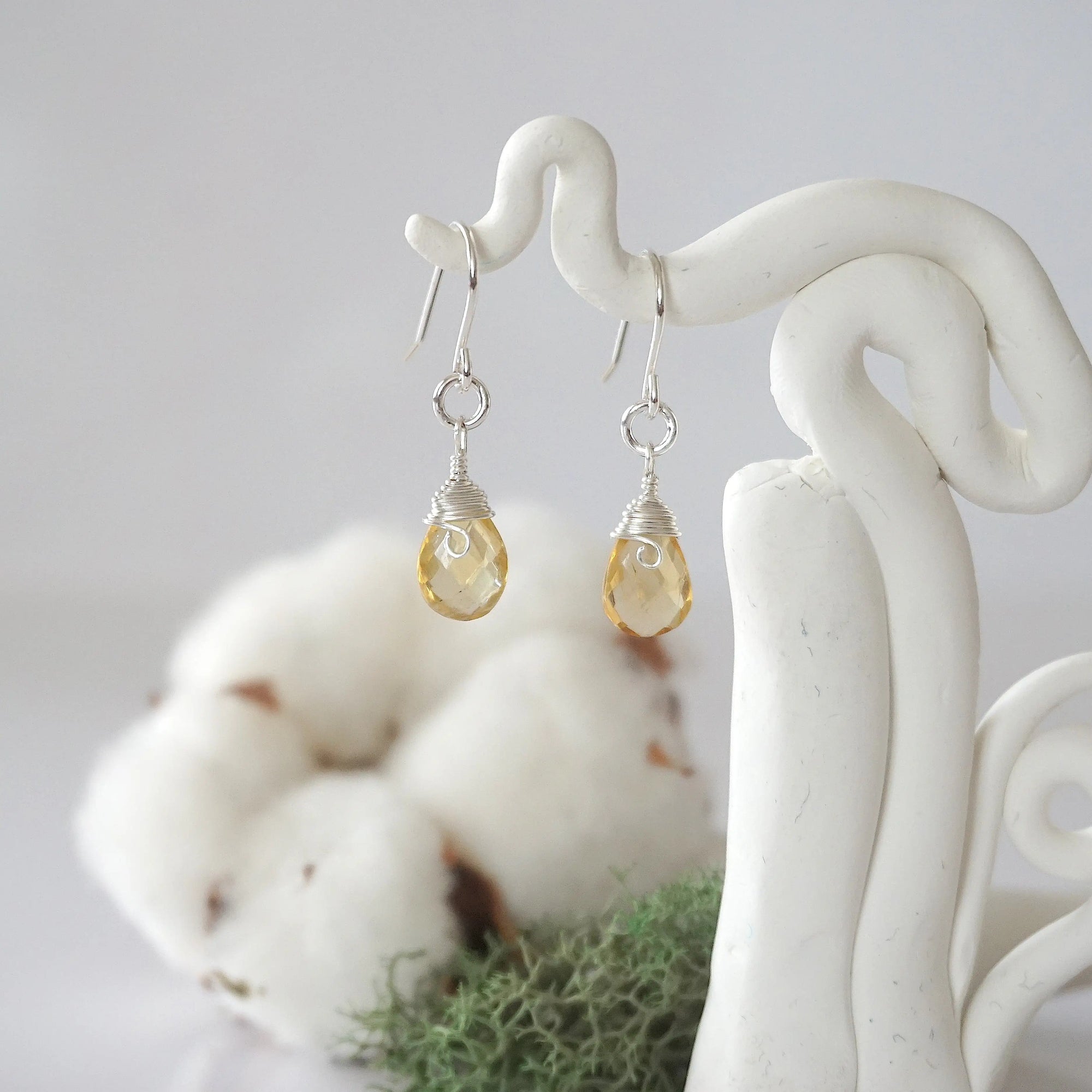 Detailed front view of handcrafted citrine sterling silver drop earrings with natural faceted citrine, artisan wire wrapping, hanging from a display – Designs by Nature Gems