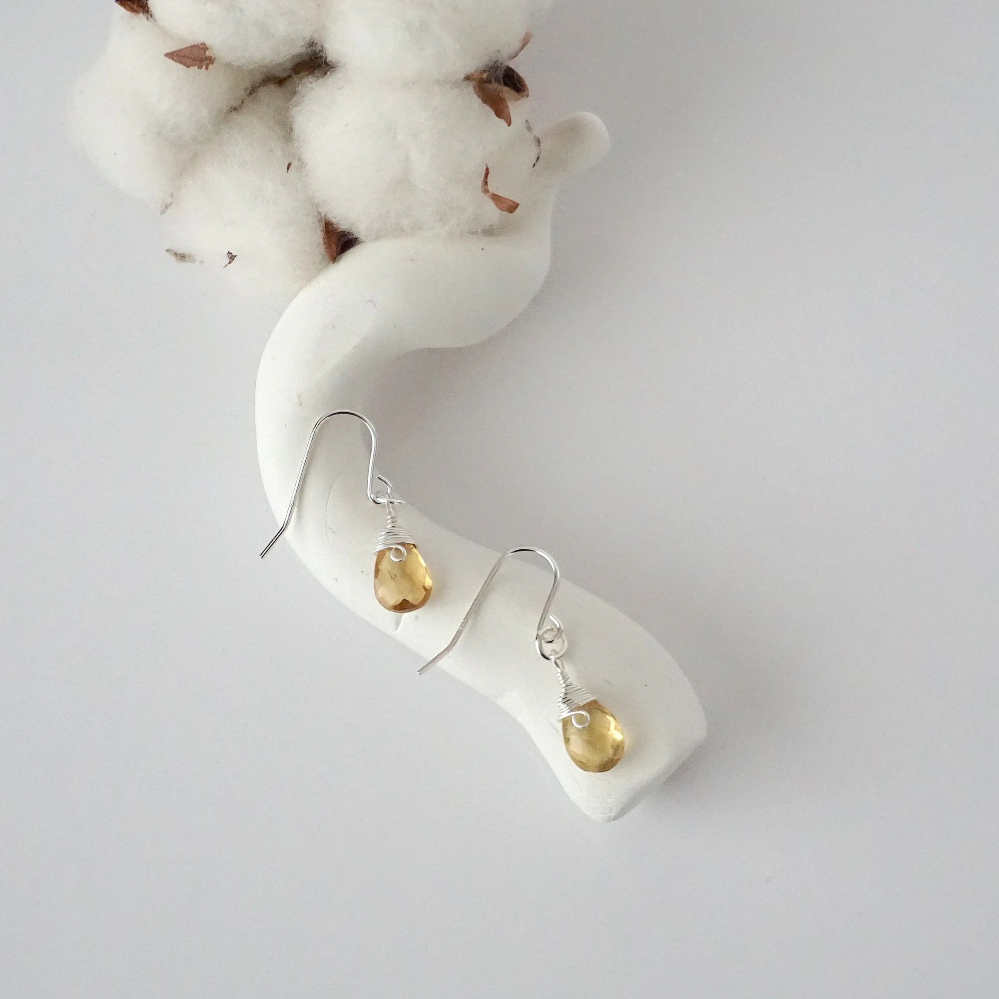 Citrine sterling silver drop earrings with faceted natural citrine stones and wire wrapping, laying flat on a display – Designs by Nature Gems