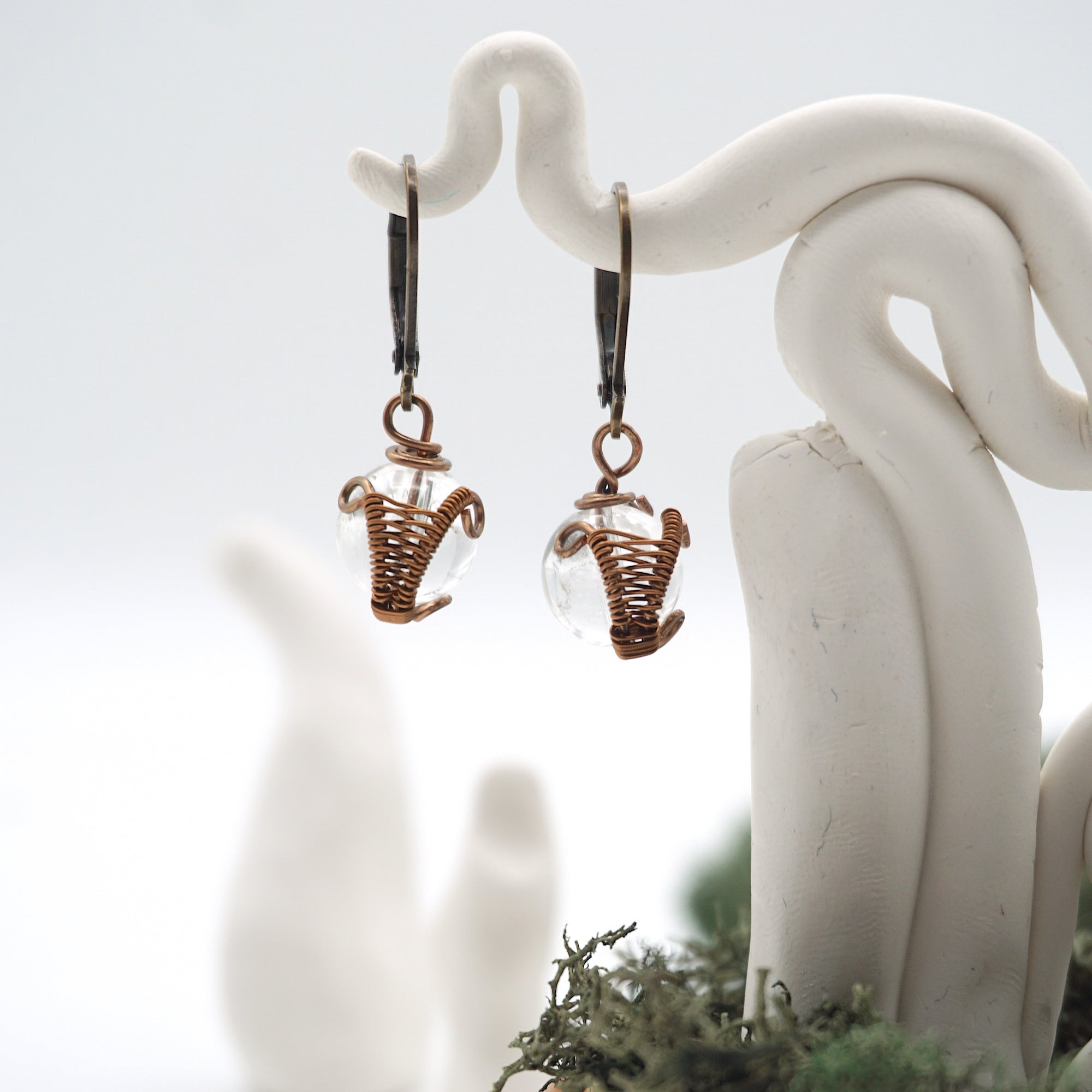 Close-up of handcrafted clear quartz drop earrings with antique bronze copper wire wrapping.