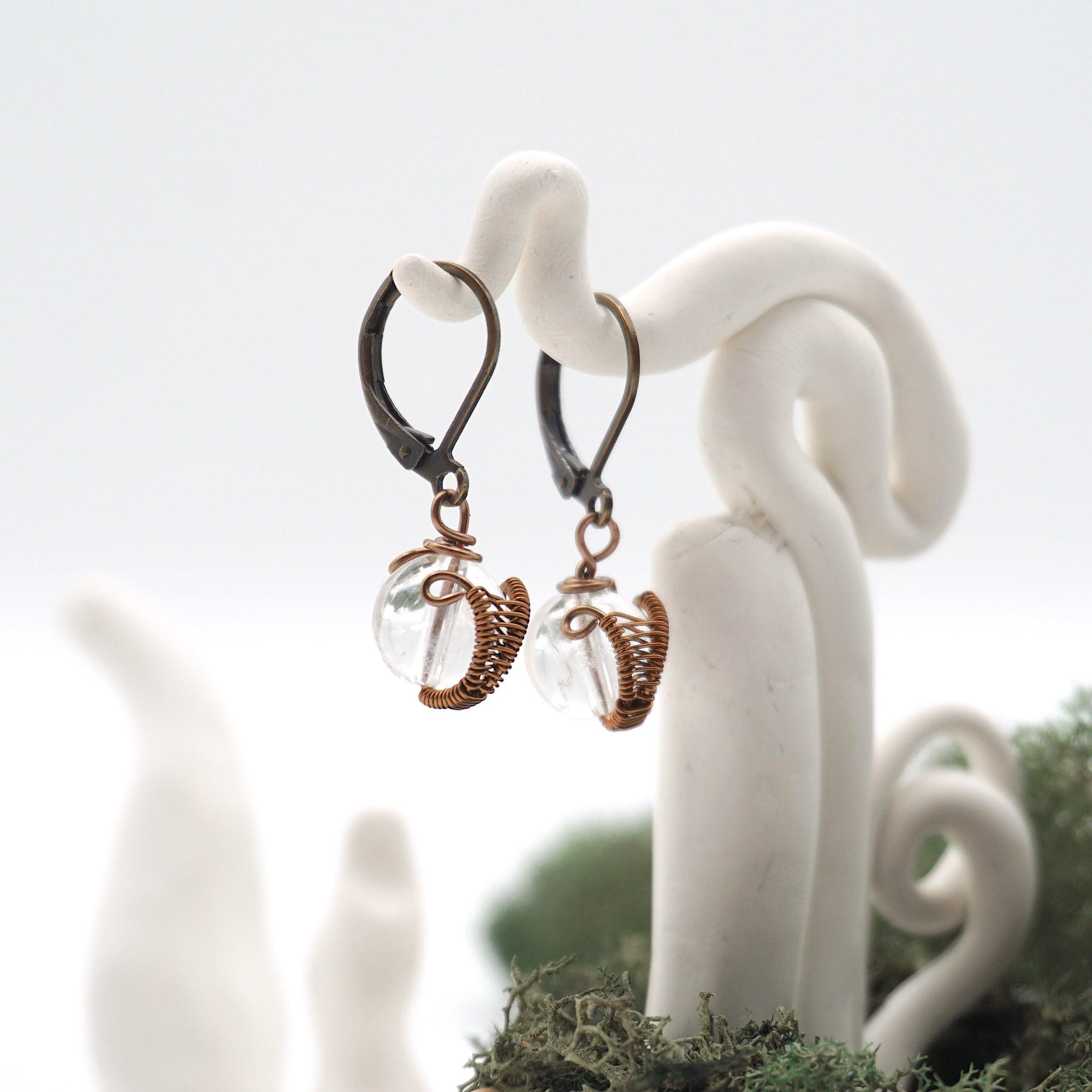 Side angle of clear quartz drop earrings on a display stand, highlighting antique bronze copper wire wrapping.