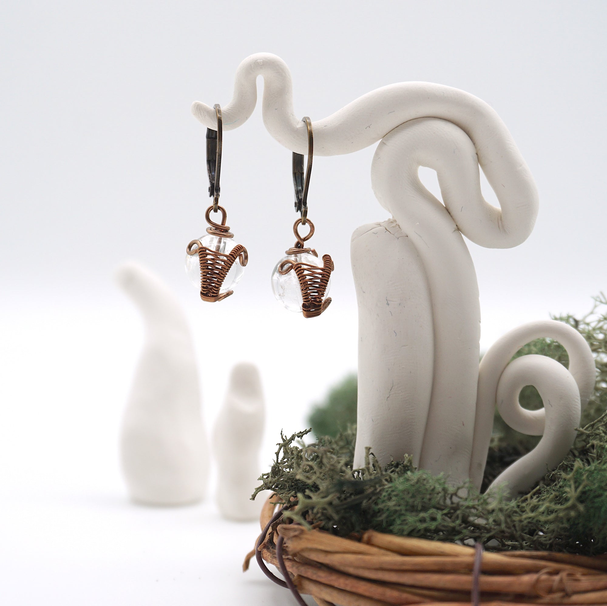 Front angle of clear quartz drop earrings hanging on a jewelry display, wire-wrapped design.