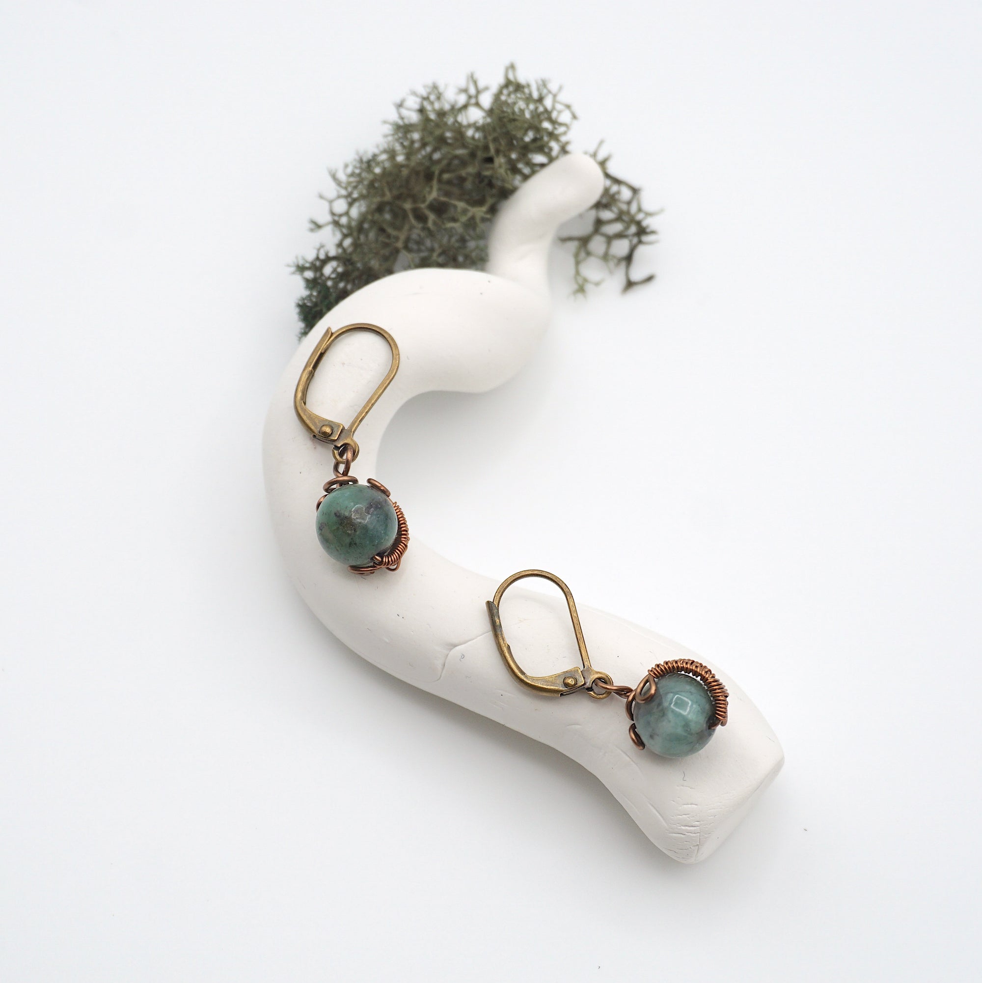 Bird’s eye view of emerald drop earrings laying flat on a display, showing detailed wire wrapping and gemstone color.