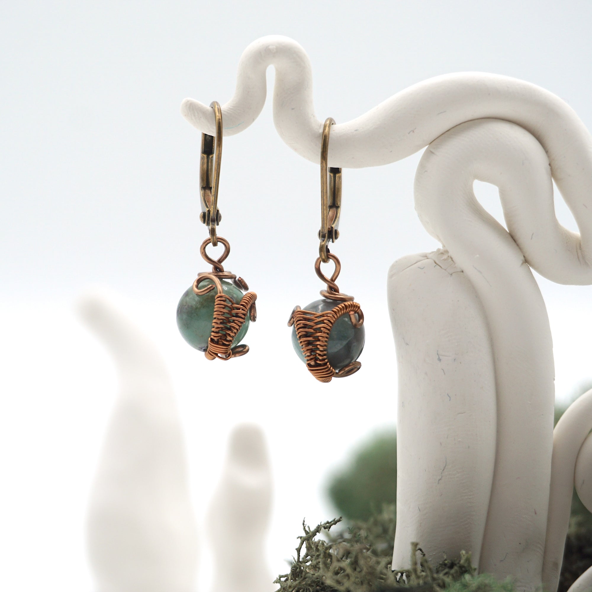 Close-up of handcrafted emerald drop earrings with antique bronze copper wire wrapping.