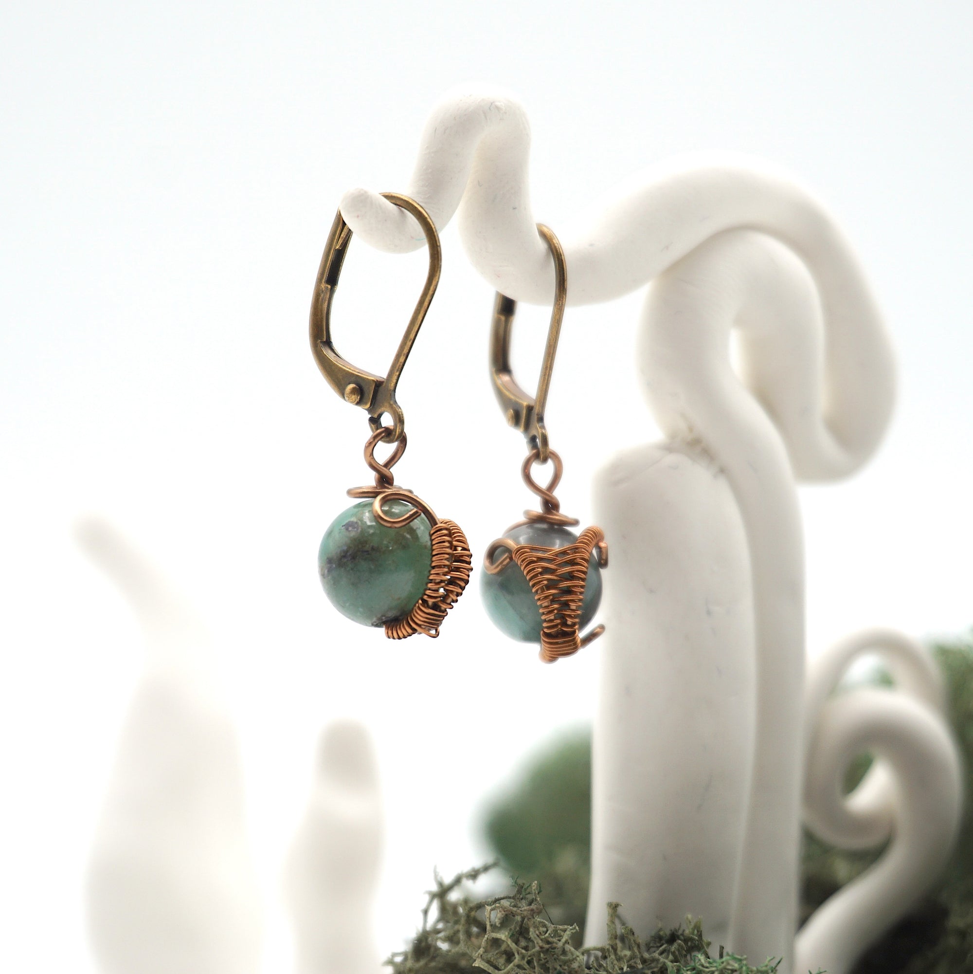 Side angle of emerald drop earrings on a display stand, highlighting antique bronze copper wire wrapping.