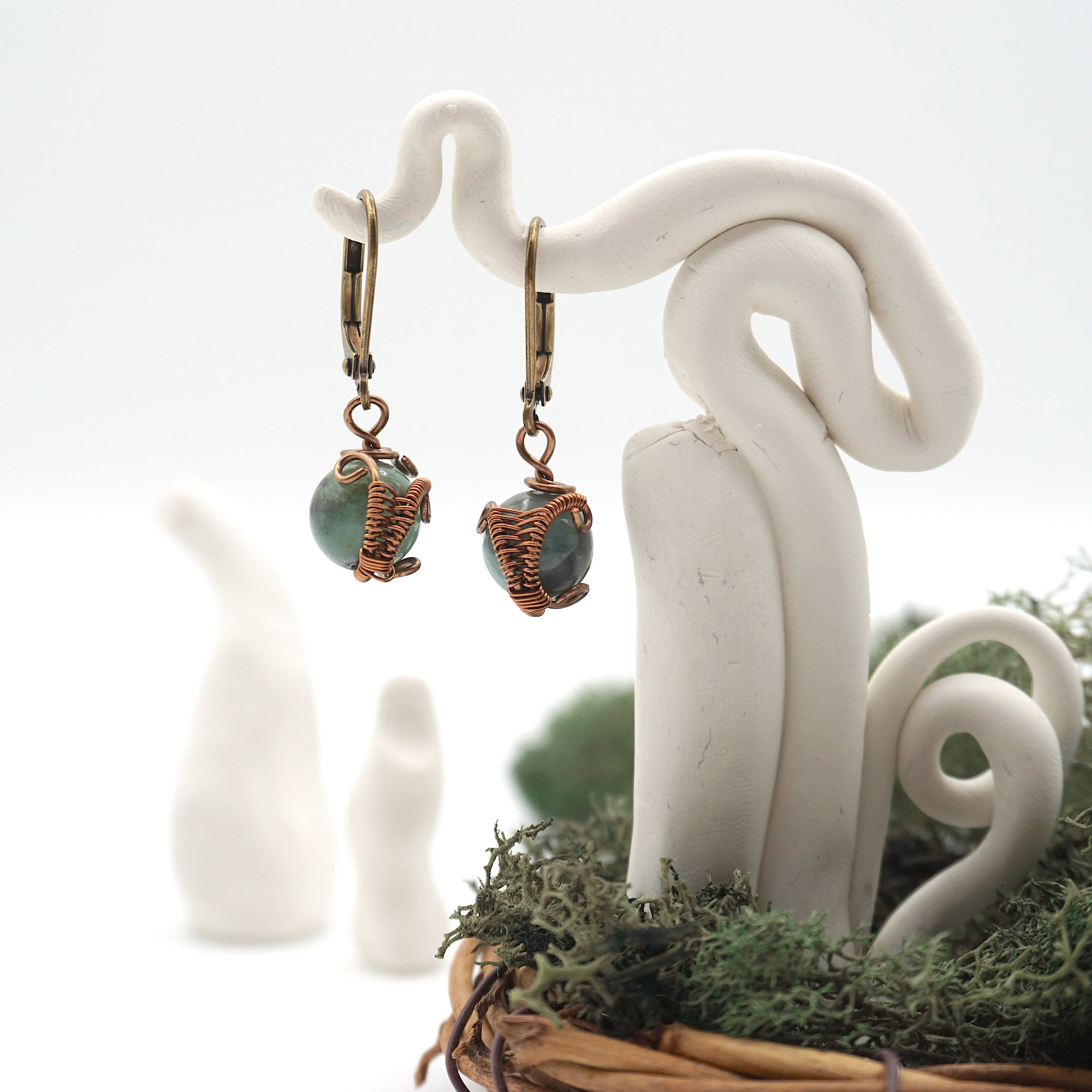 Front angle of emerald drop earrings hanging on a jewelry display, wire-wrapped design.