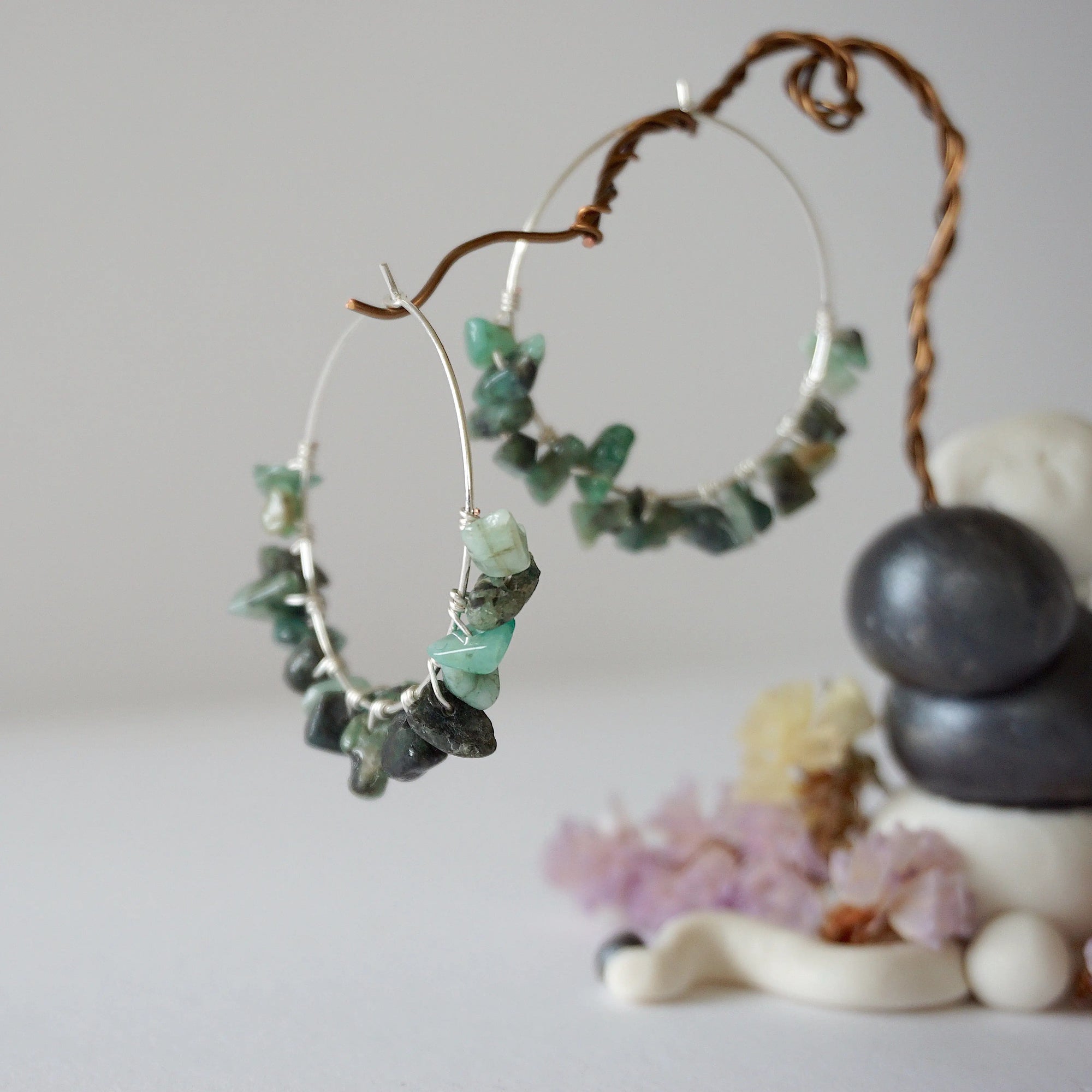 Close-up of emerald hoop earrings showing natural emerald chips and artisan wire wrapping in soft silver copper