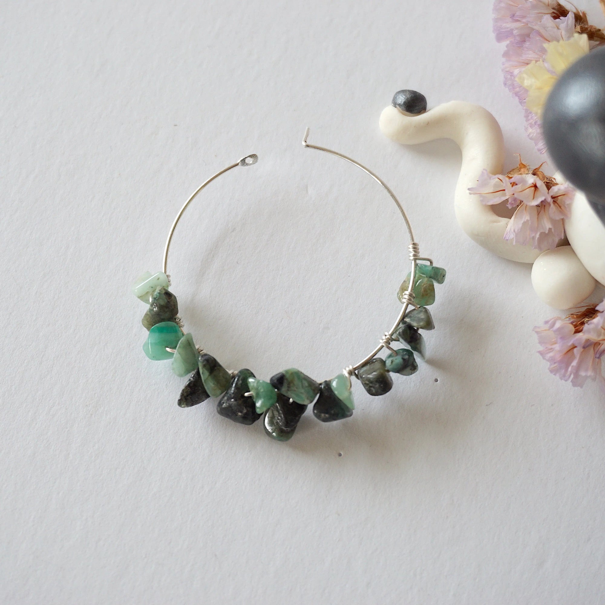 Emerald hoop earrings on flat surface with detailed view of hoop shape, natural emerald stones, and handcrafted wrapping