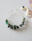Emerald hoop earrings on flat surface with detailed view of hoop shape, natural emerald stones, and handcrafted wrapping