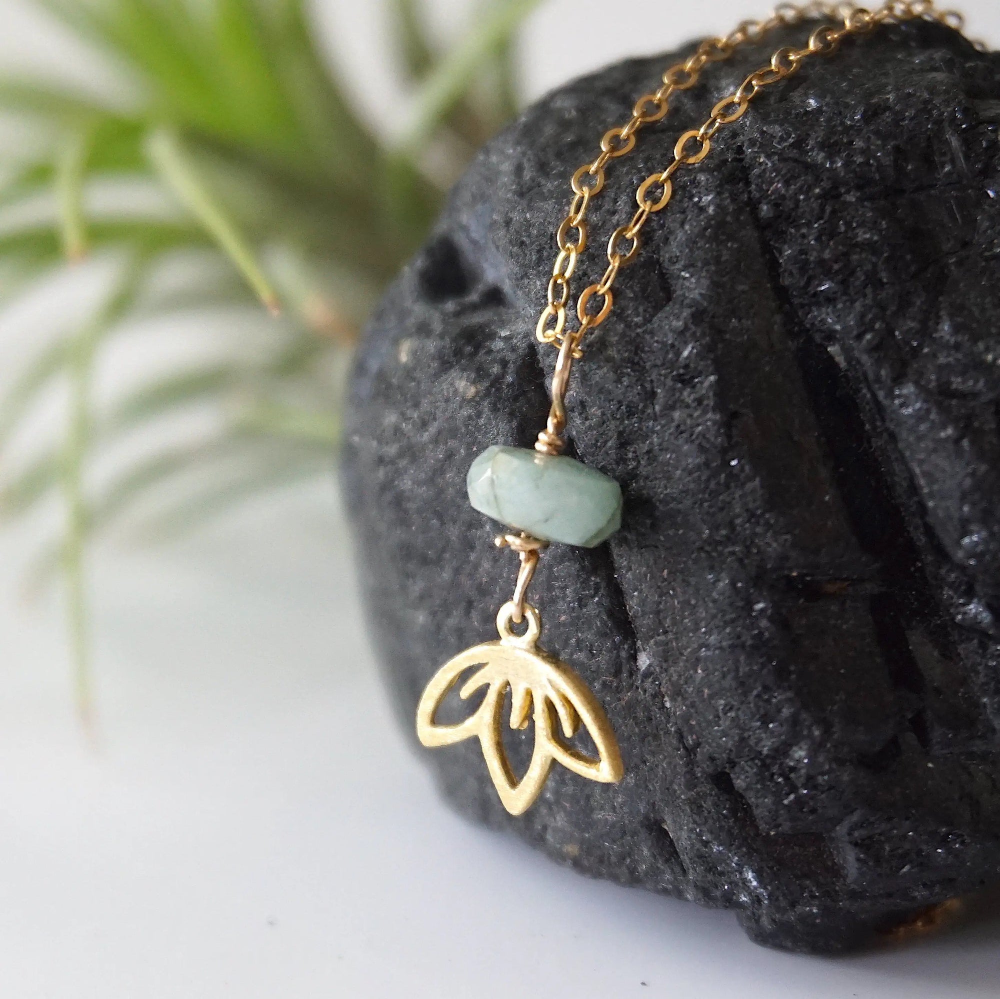 Left angle detail of emerald and lotus necklace for women with natural faceted emerald bead and minimalist lotus charm