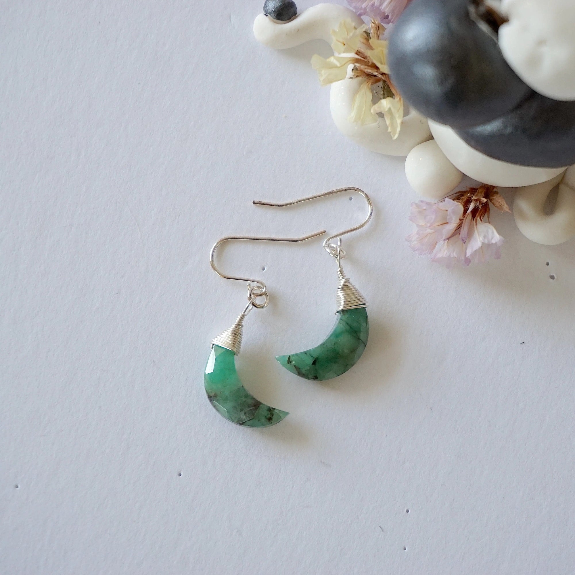 Emerald moon drop earrings in 925 sterling silver displayed on a flat surface with natural faceted crescent moon emeralds.