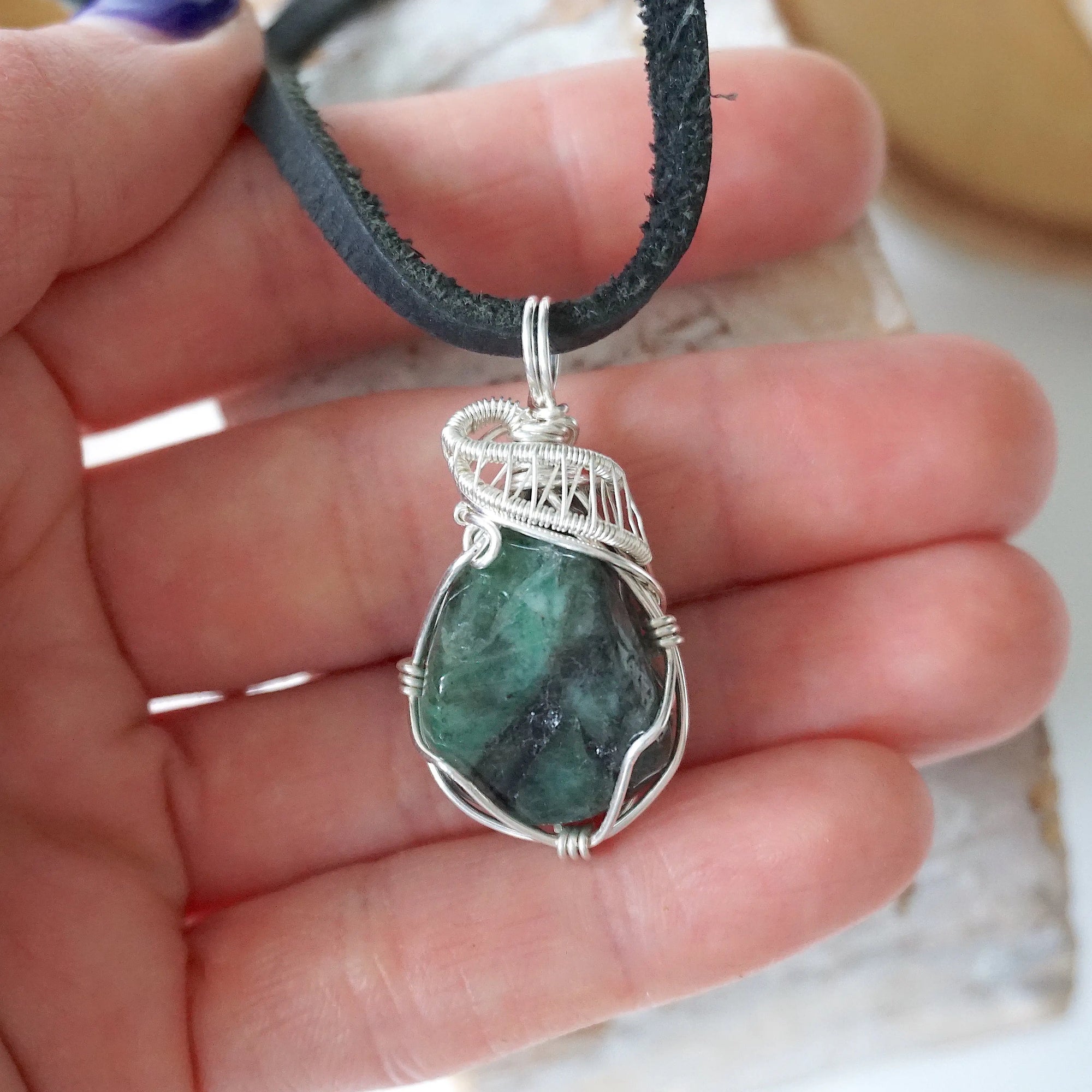 Emerald pendant for men shown in hand for size reference with natural polished-raw emerald and sterling silver wire wrap.