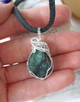 Emerald pendant for men shown in hand for size reference with natural polished-raw emerald and sterling silver wire wrap.