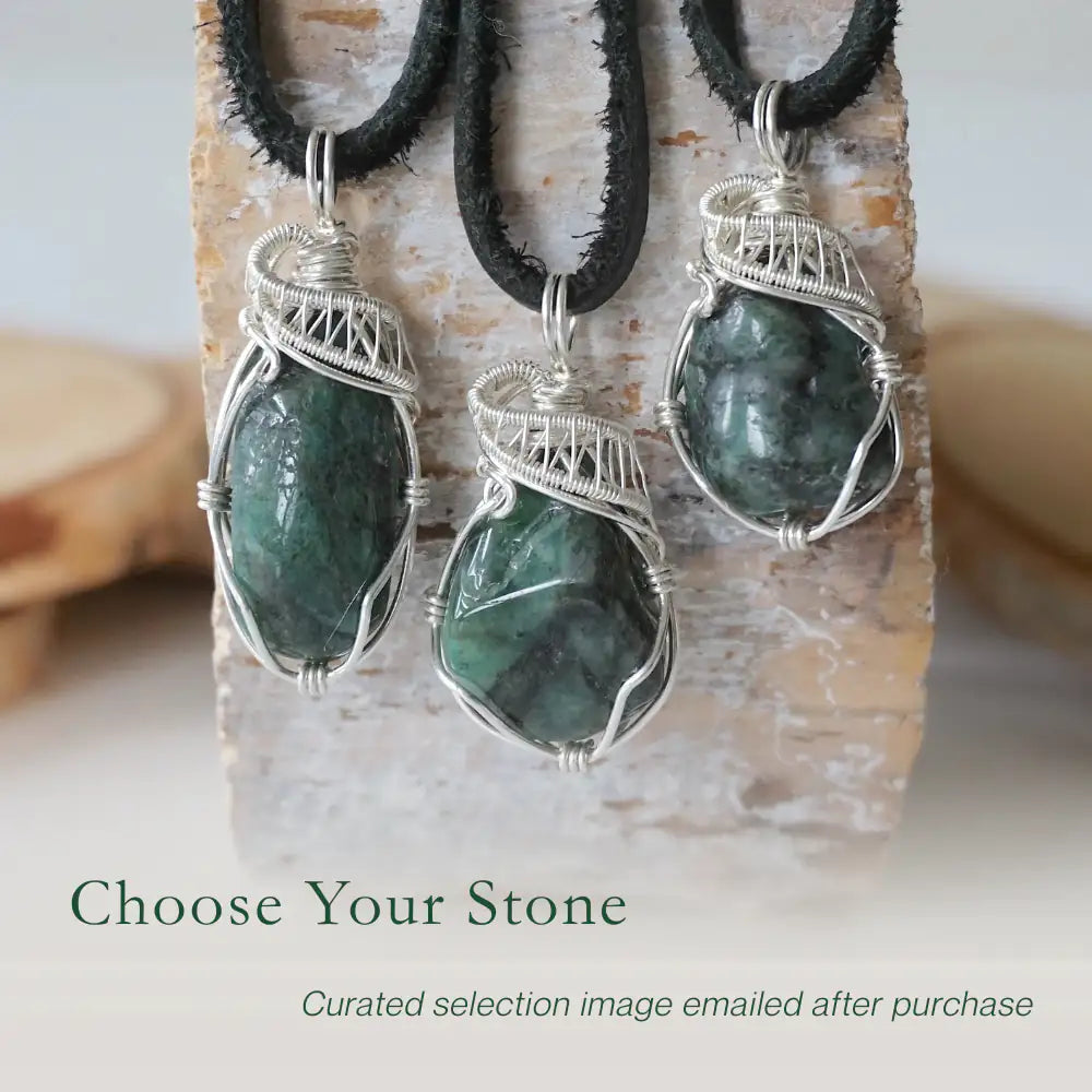 Three emerald pendants for men showing natural variation in size, shape, and green colour with sterling silver wire wrapping.