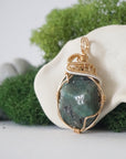 Left angle view of emerald necklace for women with natural polished-raw emerald and detailed mixed metal wire wrapping in gold filled and sterling silver