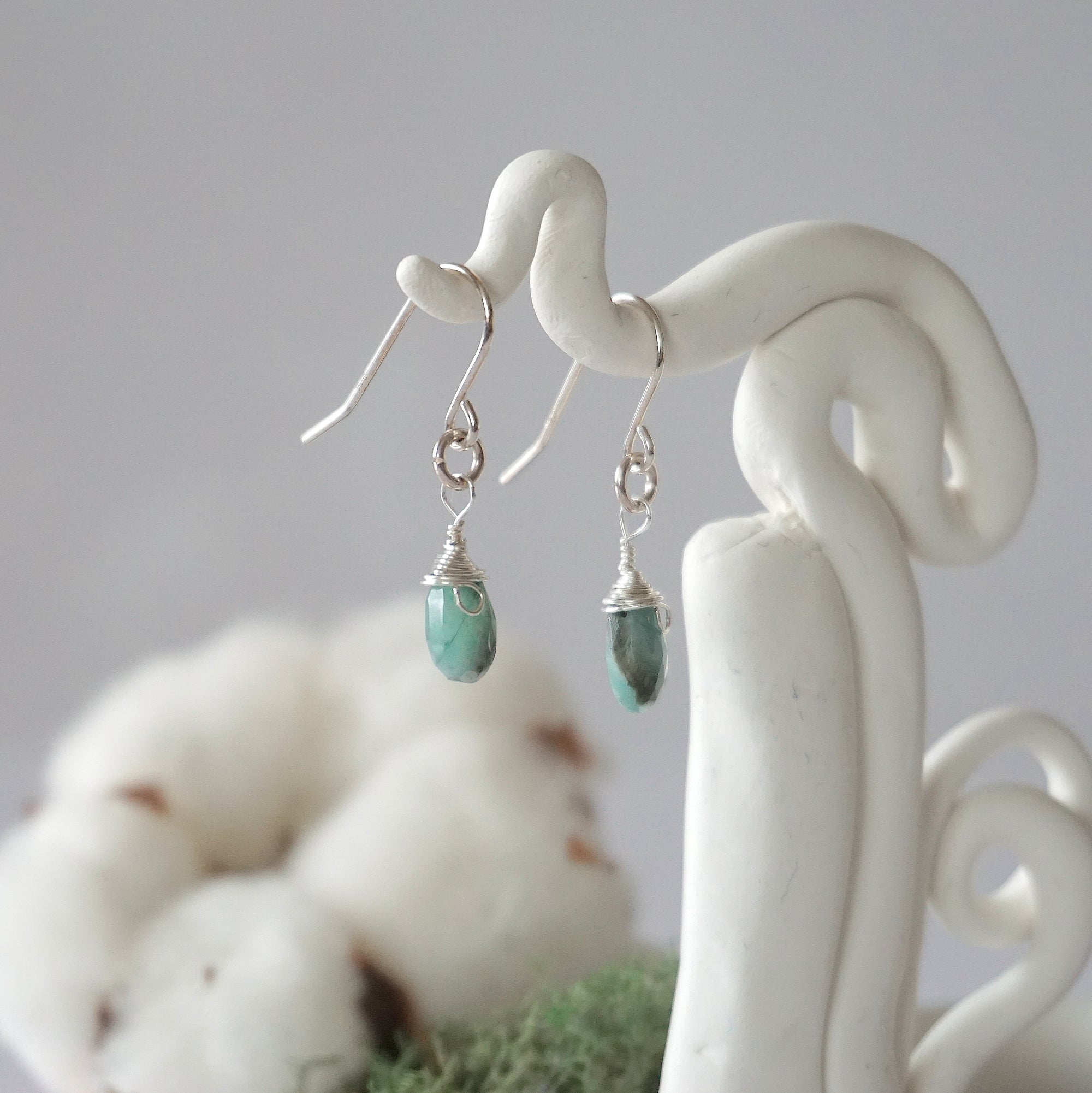 Side view of emerald sterling silver drop earrings showing wire wrapped natural faceted emerald, artisan craftsmanship, on a display – Designs by Nature Gems