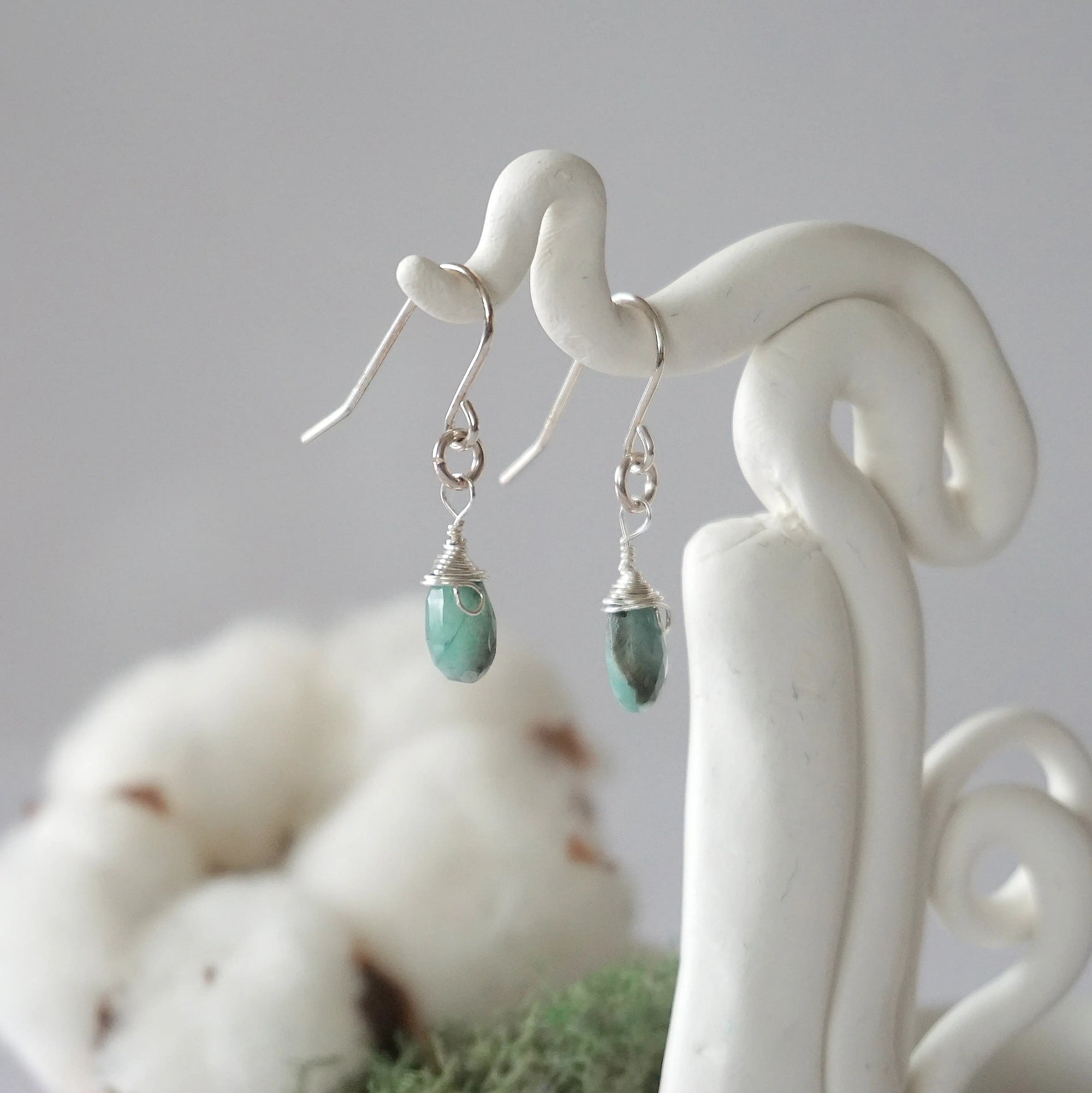 Side view of emerald sterling silver drop earrings showing wire wrapped natural faceted emerald, artisan craftsmanship, on a display – Designs by Nature Gems