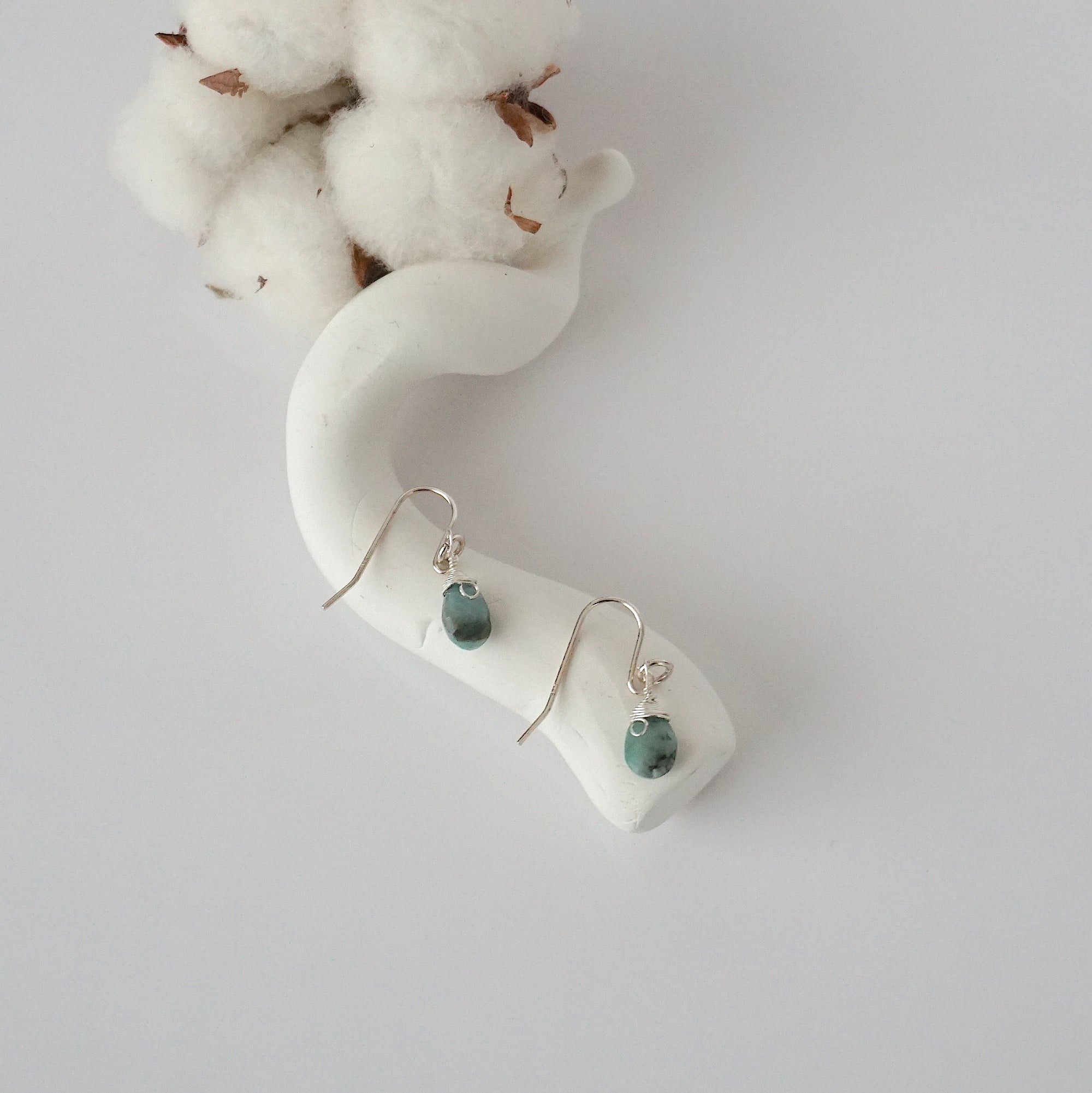 Emerald sterling silver drop earrings with faceted natural emerald stones and wire wrapping, laying flat on a display – Designs by Nature Gems