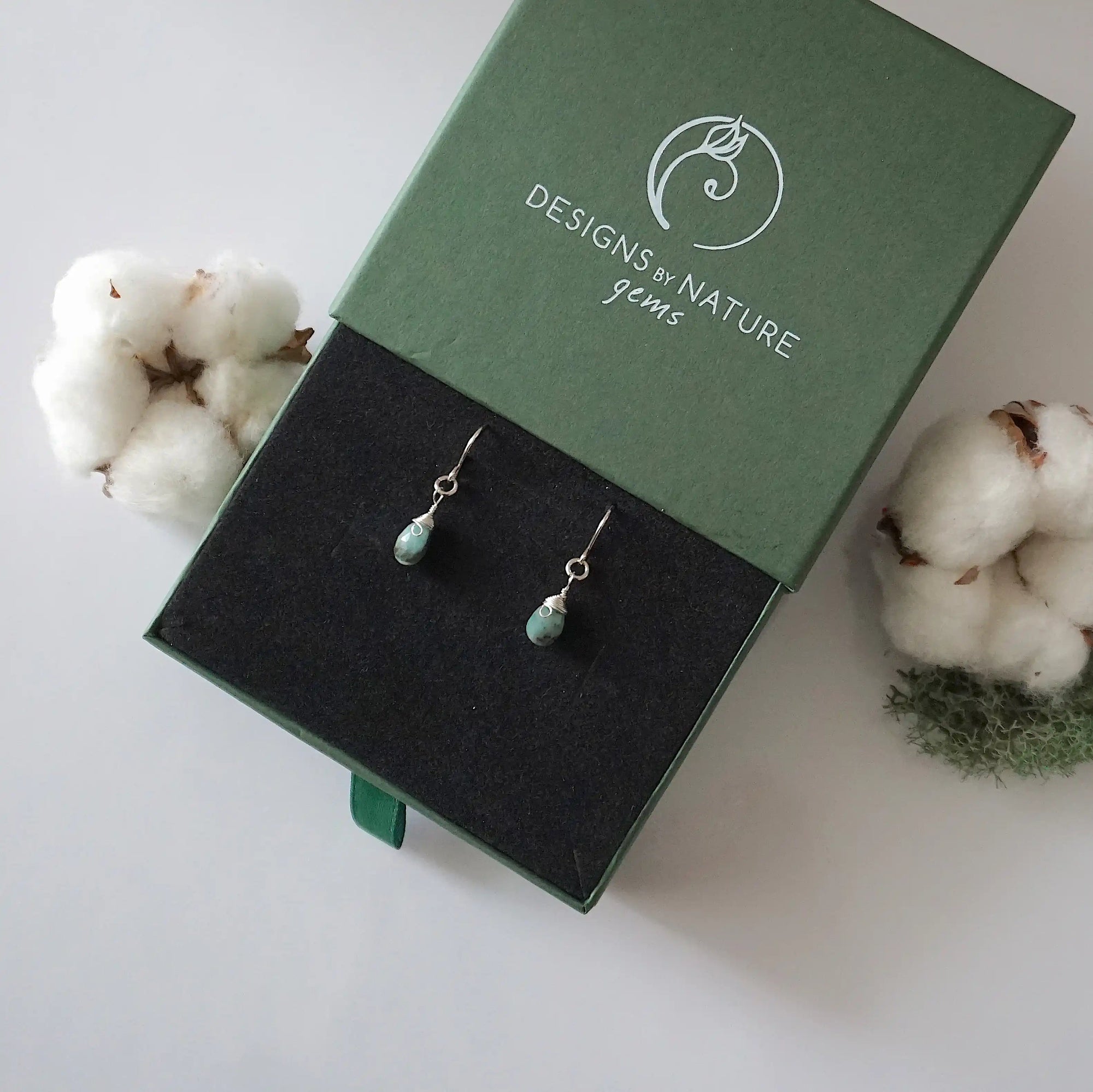 Emerald sterling silver drop earrings in branded Designs by Nature Gems jewelry box, showcasing handcrafted faceted emerald and sterling silver wire wrapping