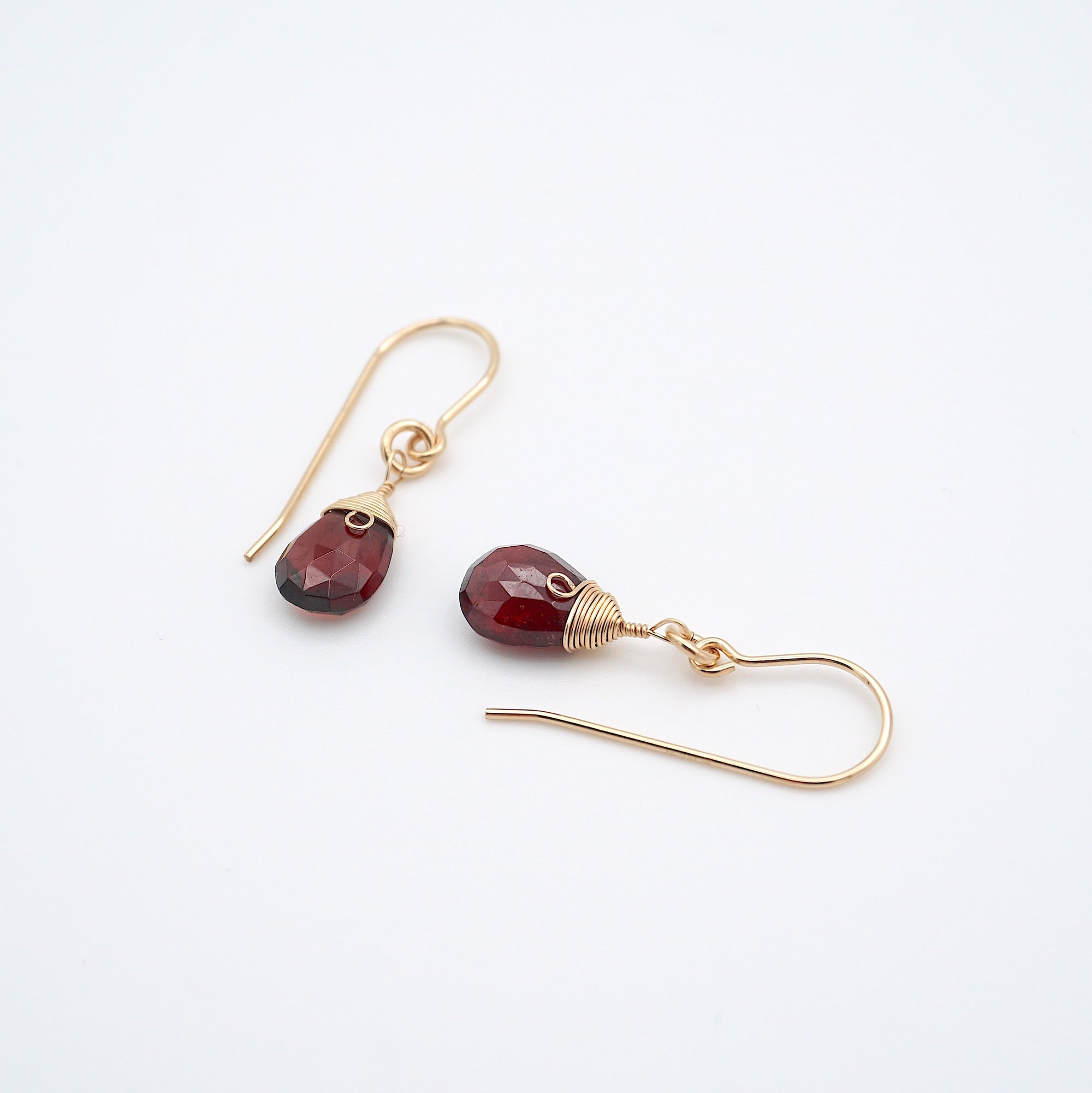 Angled flat lay of garnet 14k gold filled drop earrings with faceted red garnet stones, elegant everyday gold dangle earrings