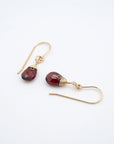 Angled flat lay of garnet 14k gold filled drop earrings with faceted red garnet stones, elegant everyday gold dangle earrings